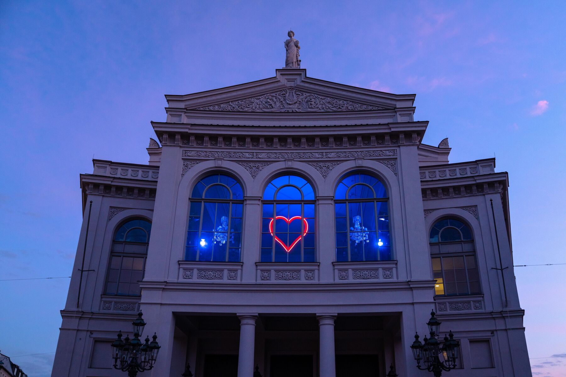 View from below of the theater building on Gärtnerplatz, with blue light shining out of the windows and a red glowing heart in the center.