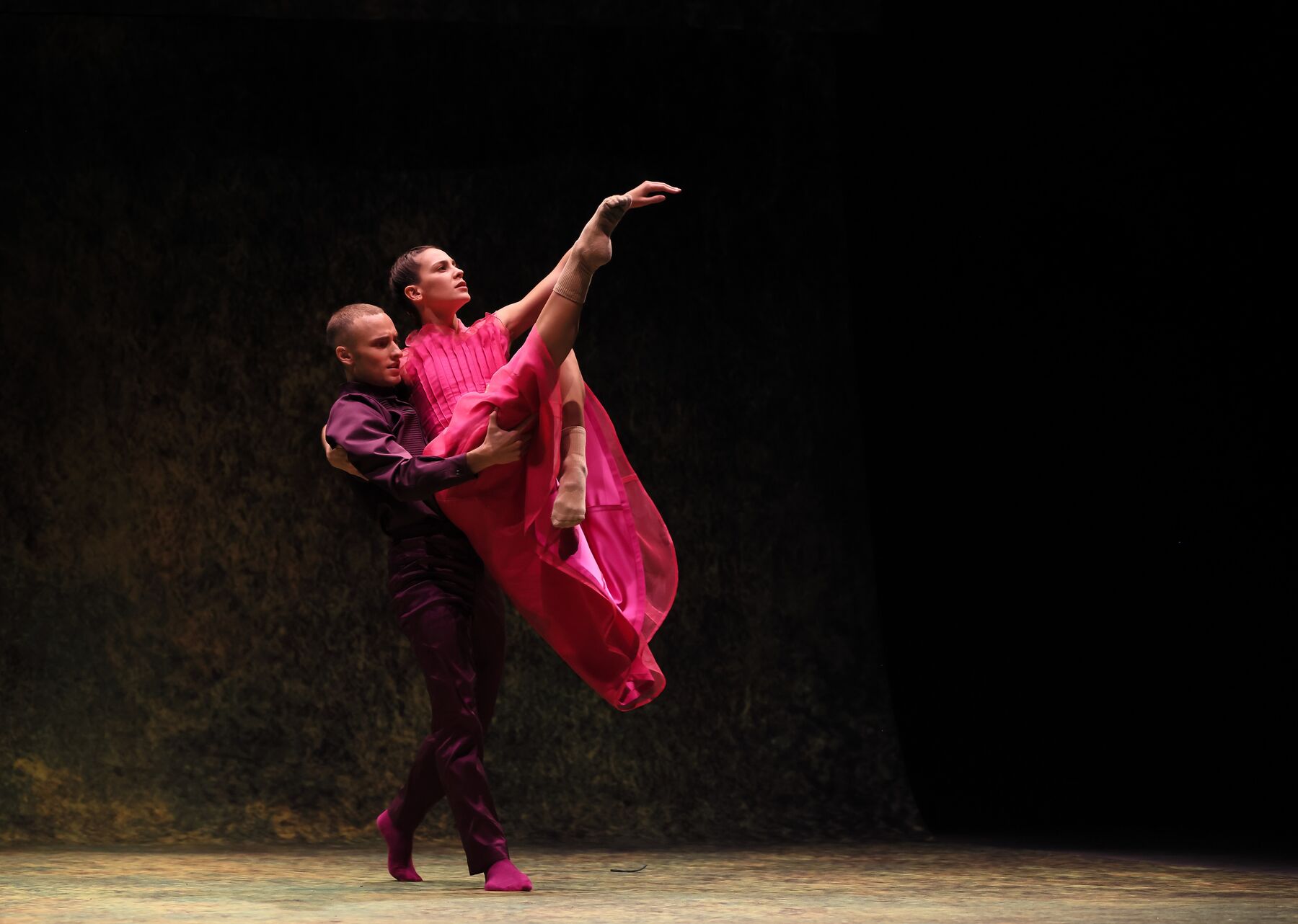 Ein Mann im lilafarbenen Gewand hält eine Frau im rosa Kleid, die ihr rechtes Bein ausstreckt.