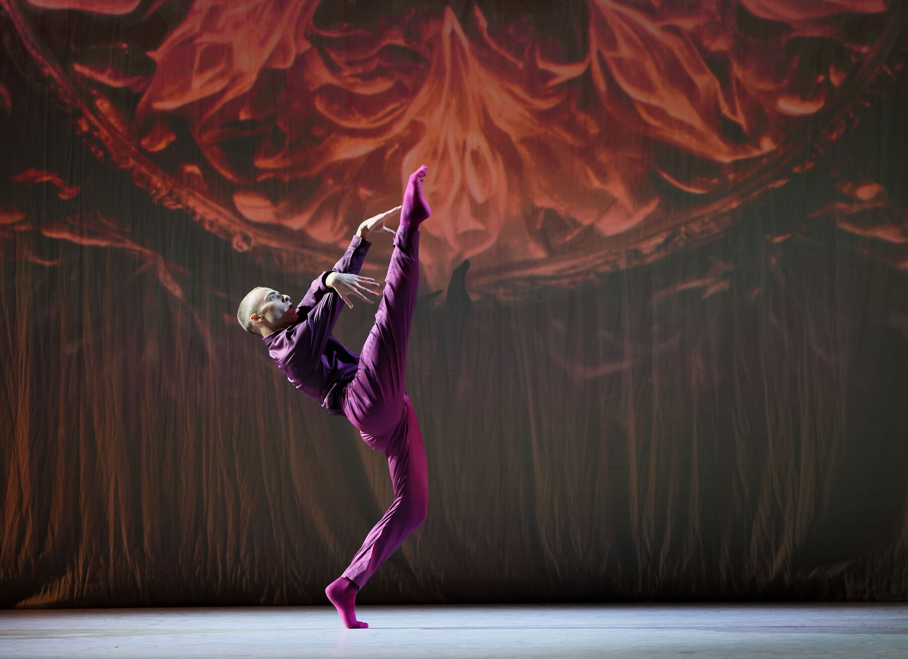 Ein Tänzer tanzt vor einer Videoinstallation. Er trägt einen dunkelroten Anzug.