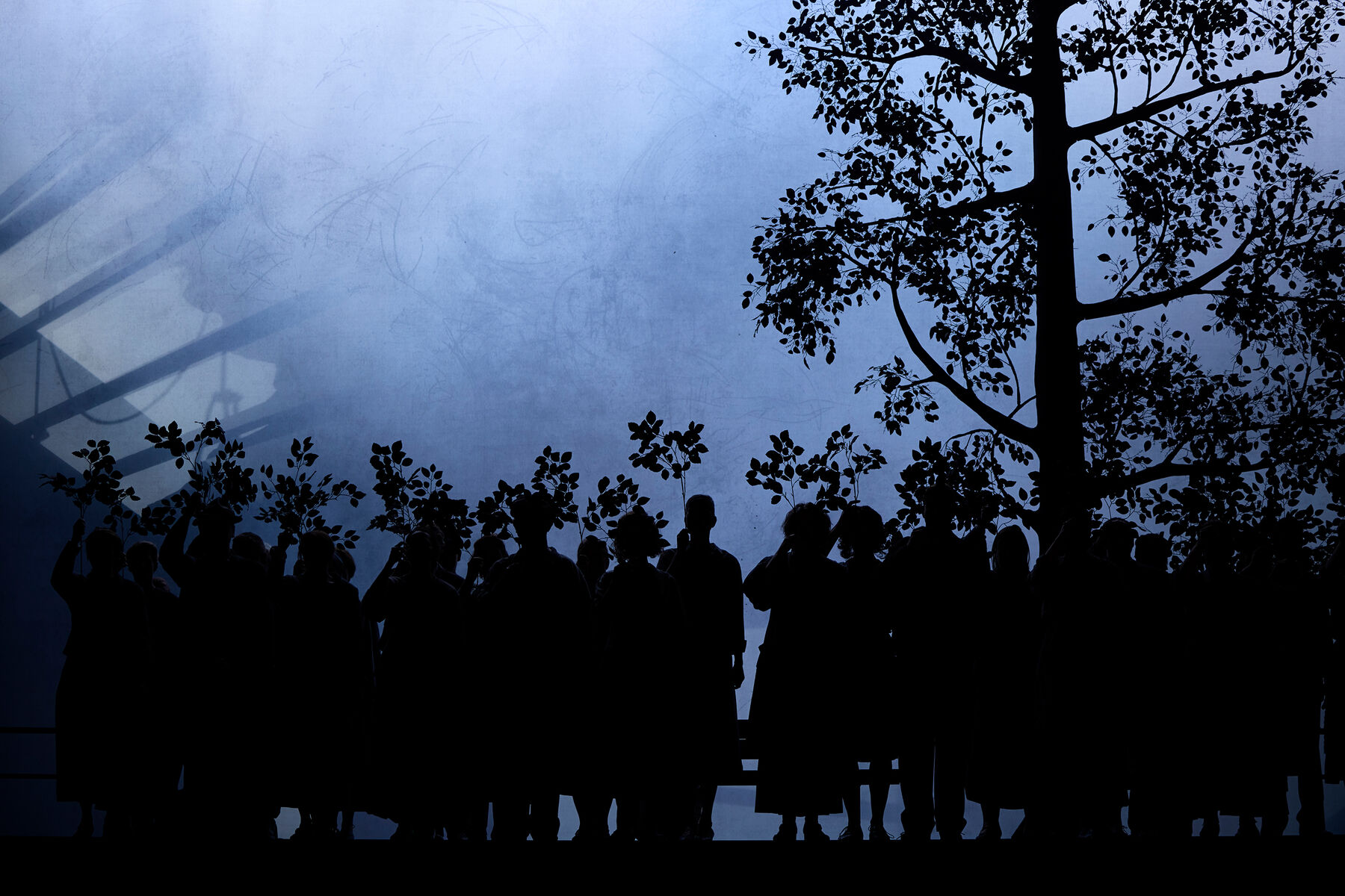 vor einem grauen nebeligen Hintergrund sieht man die Silhouette von einem Baum und Menschen die Äste in die Luft halten.
