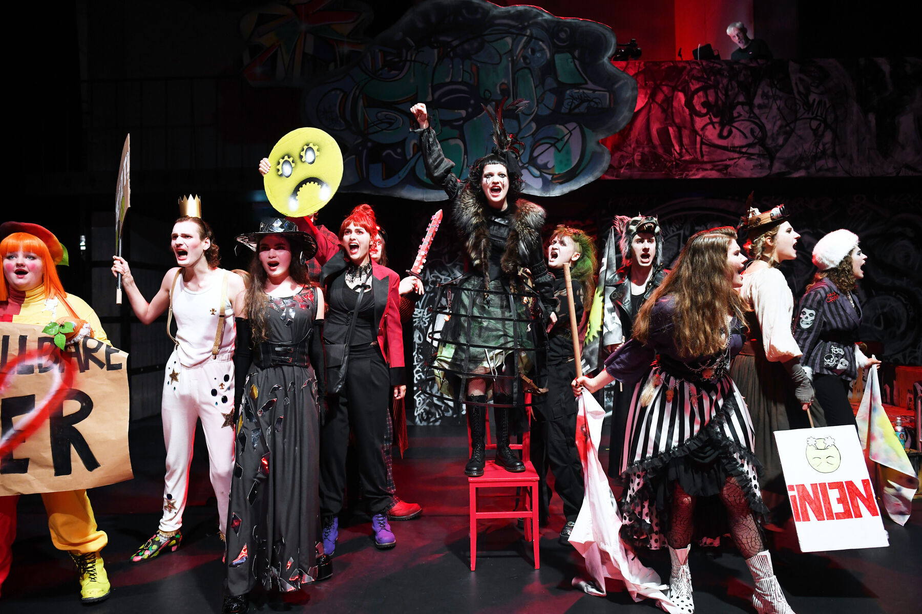 A group of young people in red and black costumes stare at the camera, screaming.