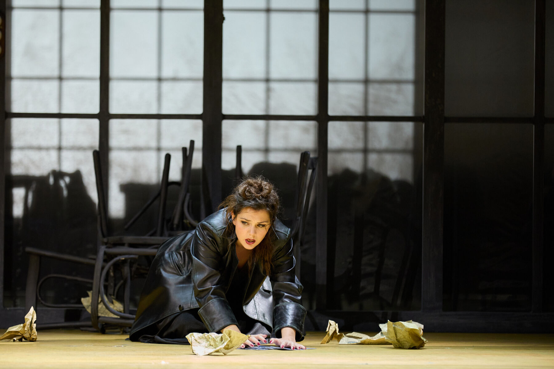 Carmen sits on the floor and picks up crumpled pieces of paper.