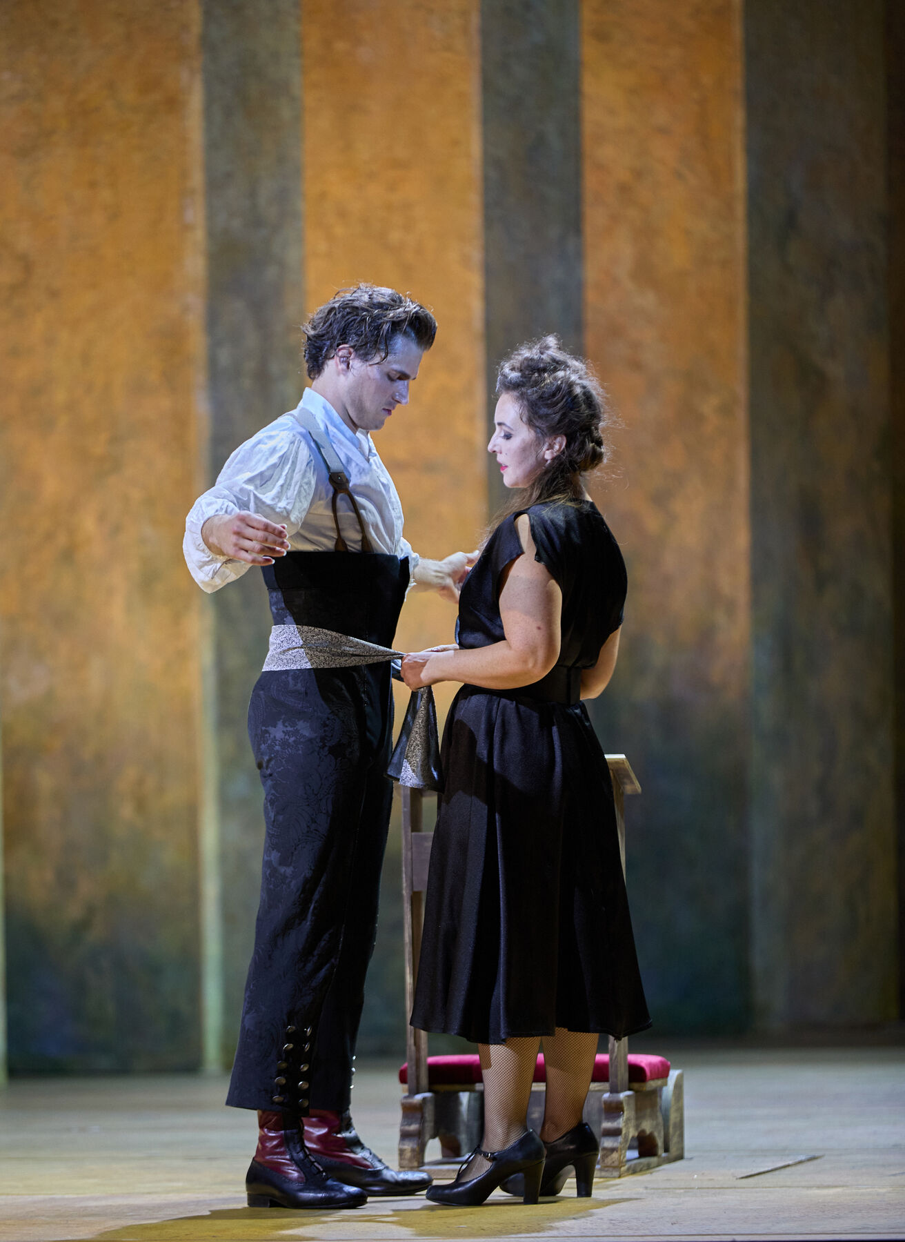 Carmen pulls Escamillo toward her with a cloth wrapped around him. He looks puzzled.