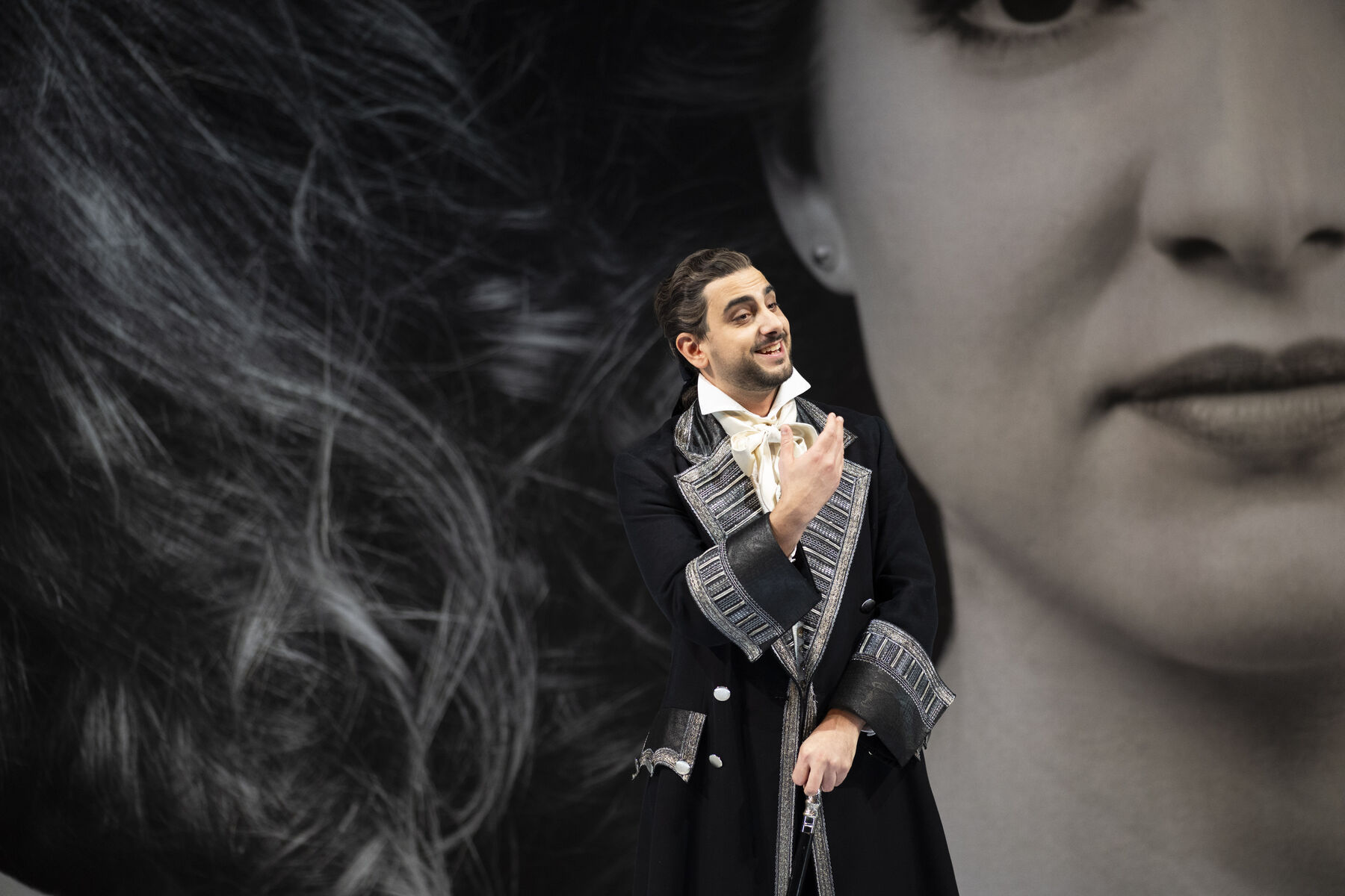 A man in an old-fashioned suit stands in front of wallpaper featuring a large image of a woman's face.