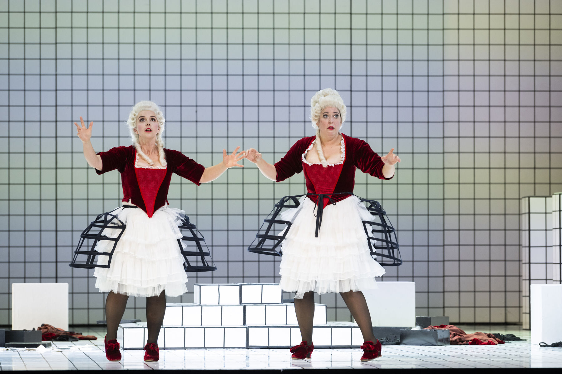 Two women wearing identical outfits consisting of red velvet dresses, black corsets and white wigs look frightened.