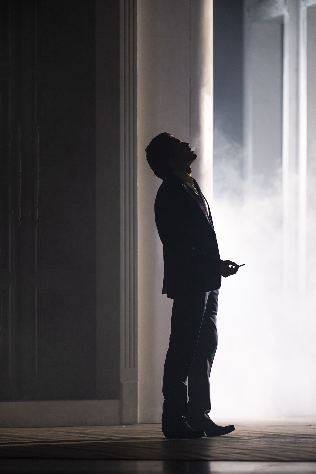 The silhouette of a man in a suit smoking can be seen. Fog rises in the background.