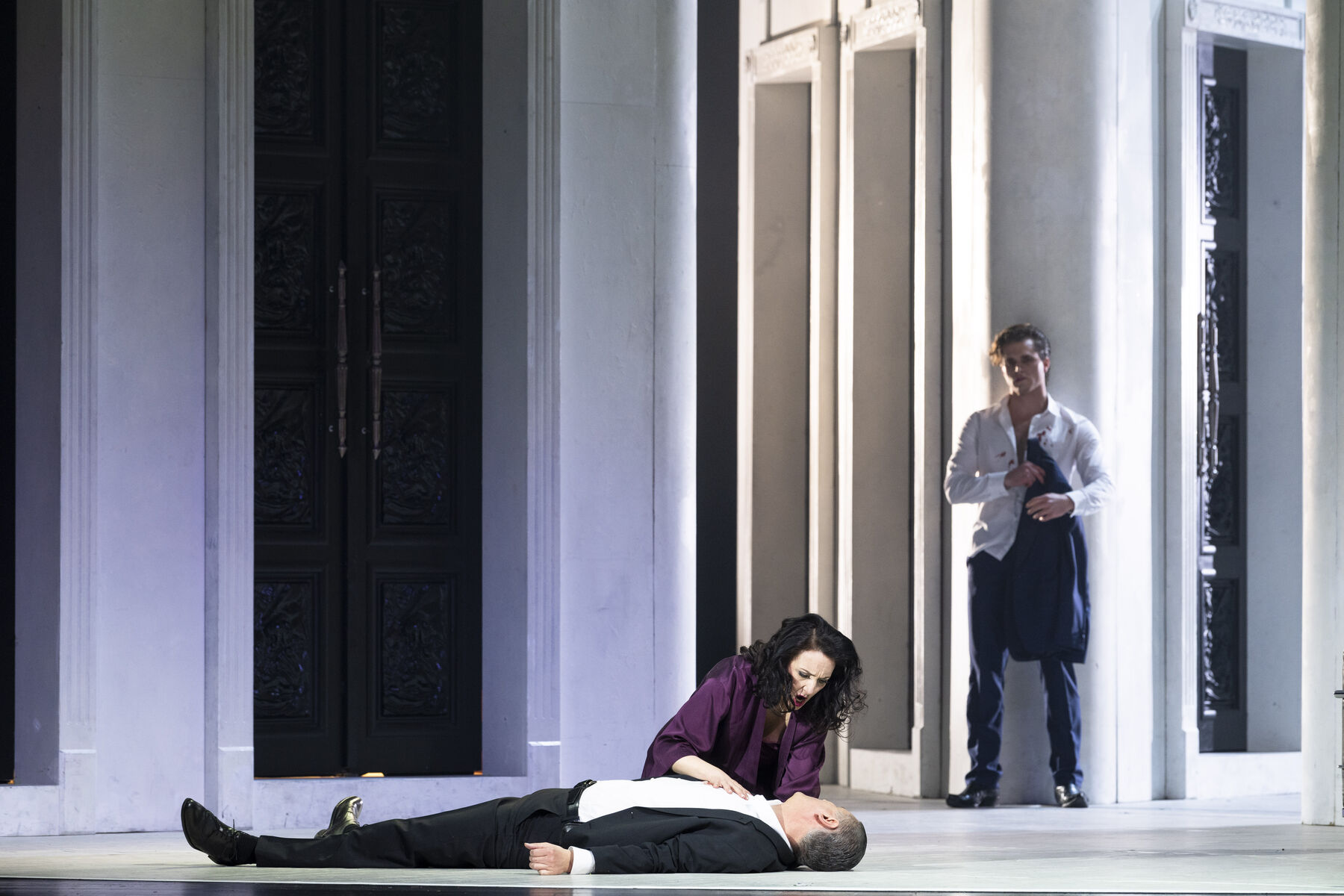 Donna Anna leans over the dead Commendatore. Don Giovanni stands in the background, leaning against a wall.