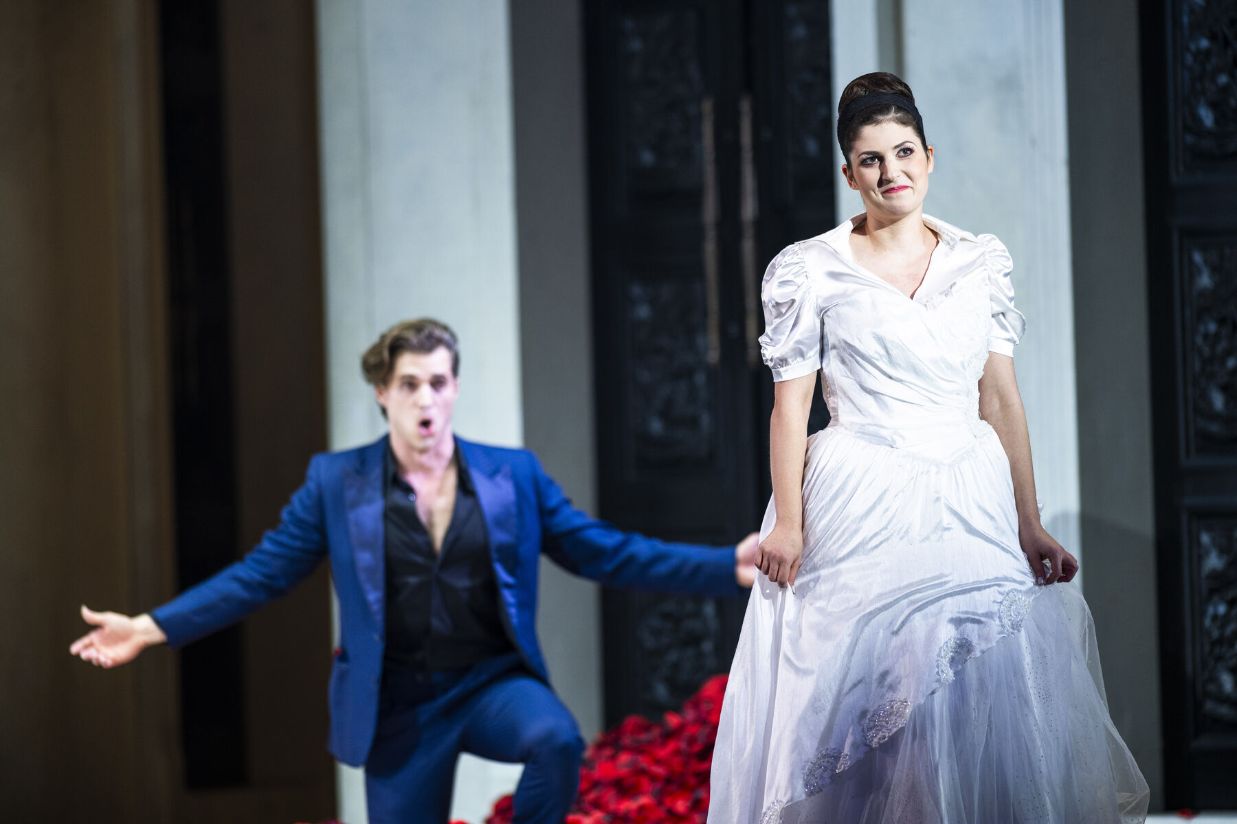 Zerlina wears a wedding dress and stands in a mountain of rose petals. Don Giovanni kneels behind her with his arms outstretched and sings.