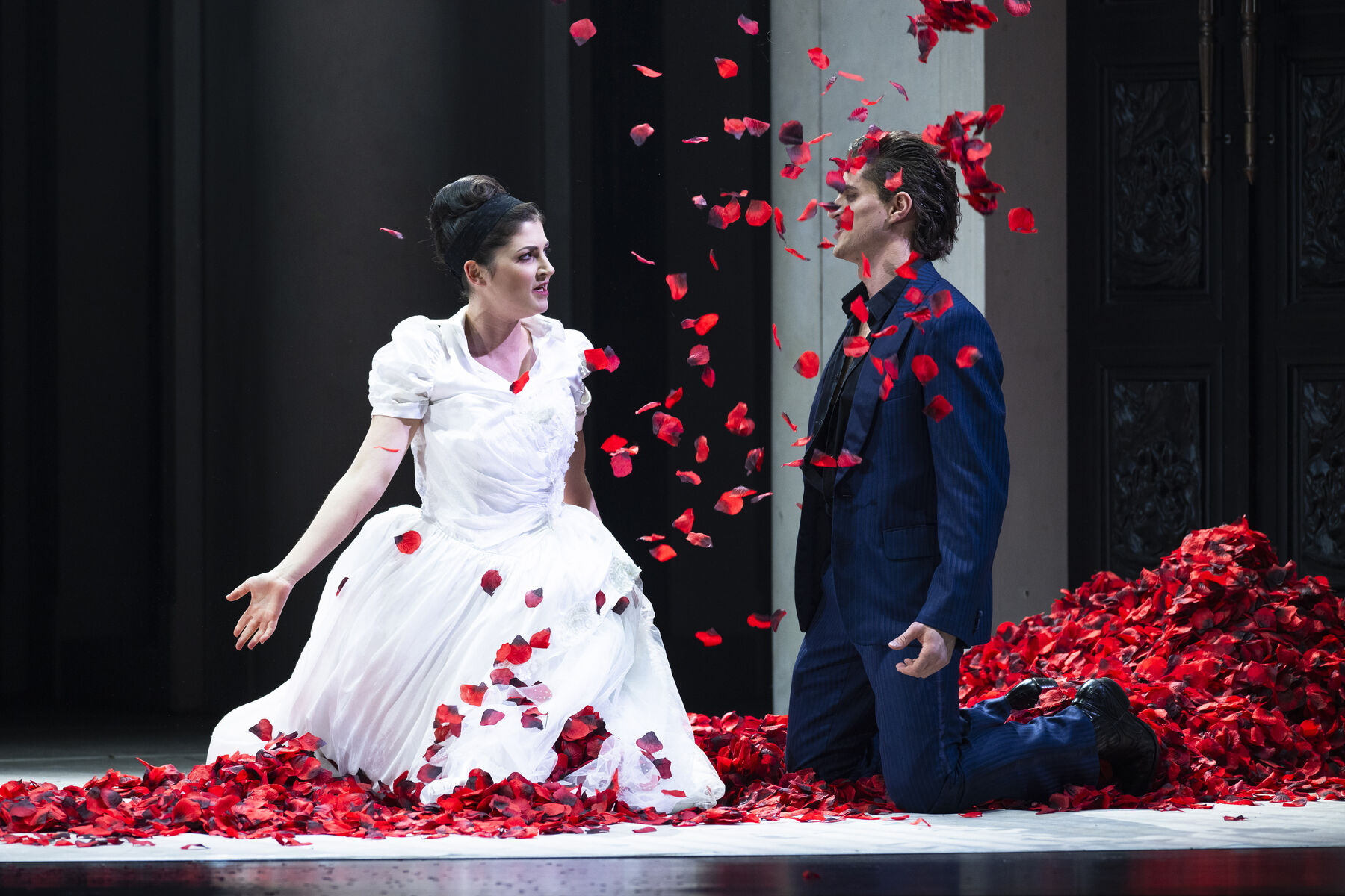 Zerlina in her wedding dress and Don Giovanni kneel in the mountain of rose petals. A flurry of petals flies through the air.