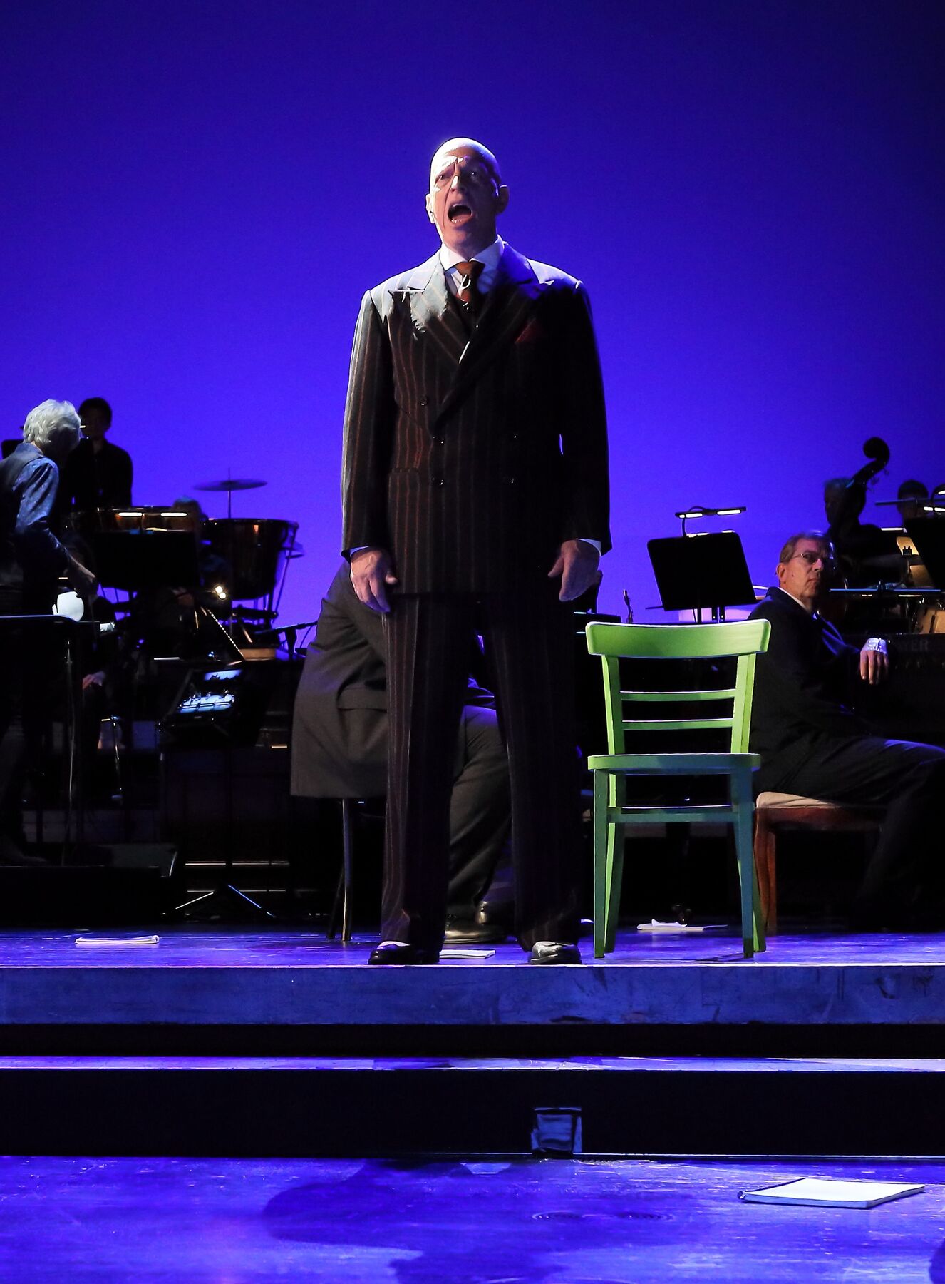 A man stands in front of a blue illuminated background against which the silhouette of a band can be seen.