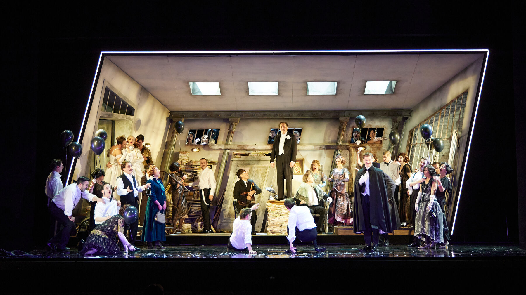 Eine Gruppe von Menschen steht in einem ärmlich anmutenden Raum. Sie halten Ballons in der Hand, lachen und feiern.