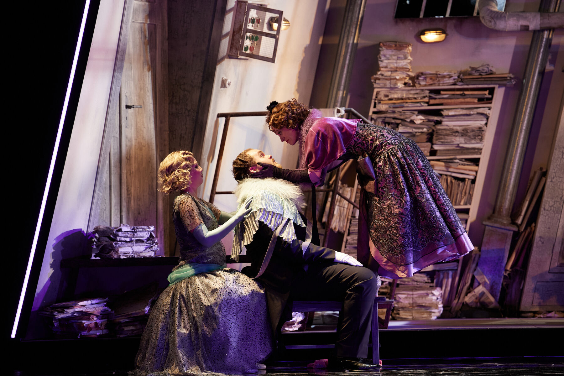 Ein Mann sitzt auf einem Stuhl. Hinter ihm sitzt eine Frau, die ihn an den Schultern hält. Vor ihm steht eine Frau, die sein Gesicht in den Händen hält.