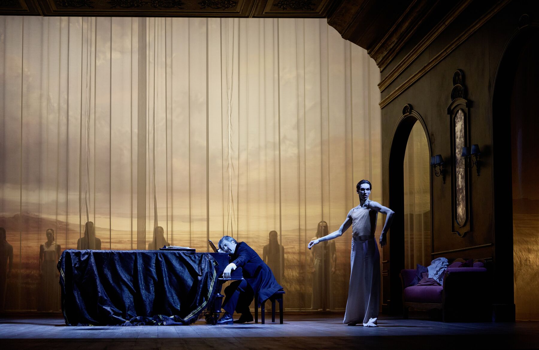 Ein Mann sitzt schlafend an einem Flügel. Schräg vor ihm steht ein Tänzer der sich anmutig bewegt. Im Hintergrund sieht man eine weite Landschaft vor der mehrere Menschen stehen.