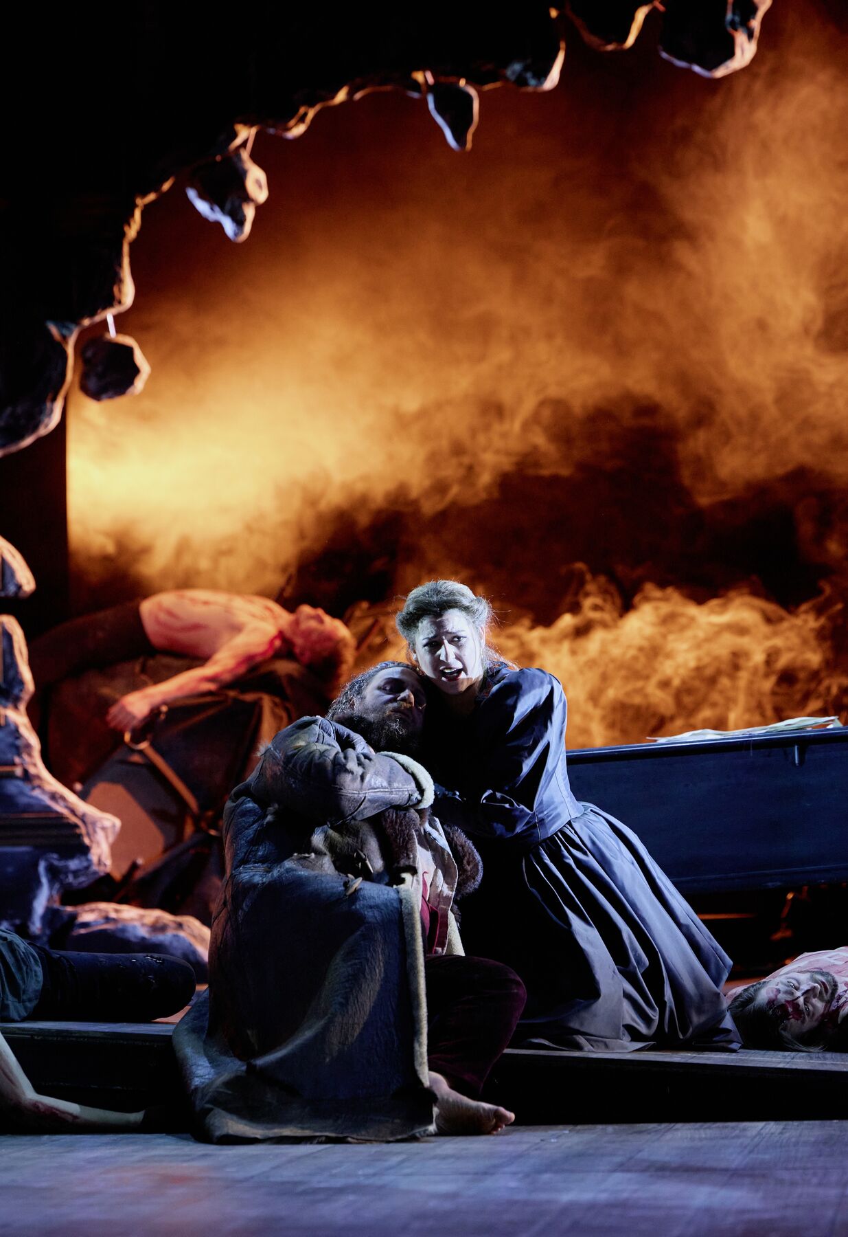 eine Frau in einem pompösen schwarzen Kleid kniet und hält einen verwundeten Mann in einem langen Mantel. im Hintergrund sieht man ein großes Loch in der Wand, welches von rotem Nebel gefüllt ist.