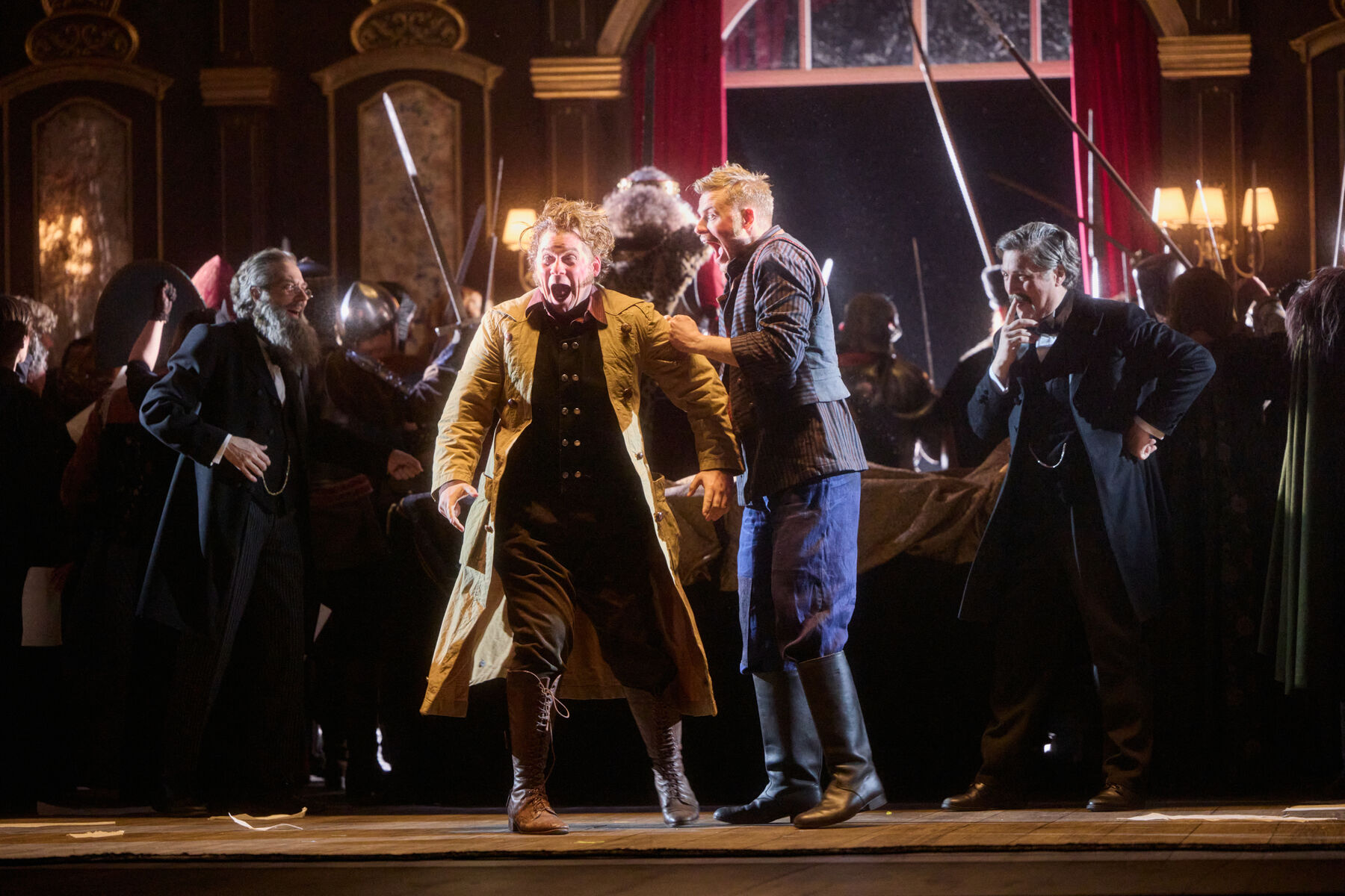 zwei Männer stehen schreiend in der Mitte. Beide tragen historische Kostüme. Der Linke hat hat zusätzlich noch einen langen gelben Mantel an. Im Hintergrund stehen Krieger mit Lanzen und zwei Männer in schwarzen Fracks. 