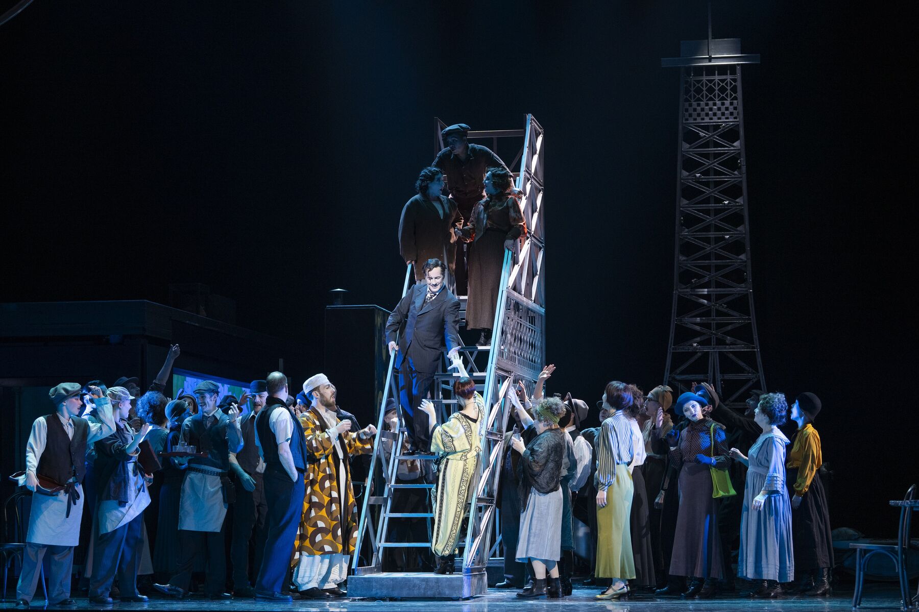 Eine Menschenmasse steht links und recht von einer Treppe. Sie schauen hoch auf einen Mann, der auf der Treppe steht. Weiter oben auf der Treppe stehen drei weitere Menschen.