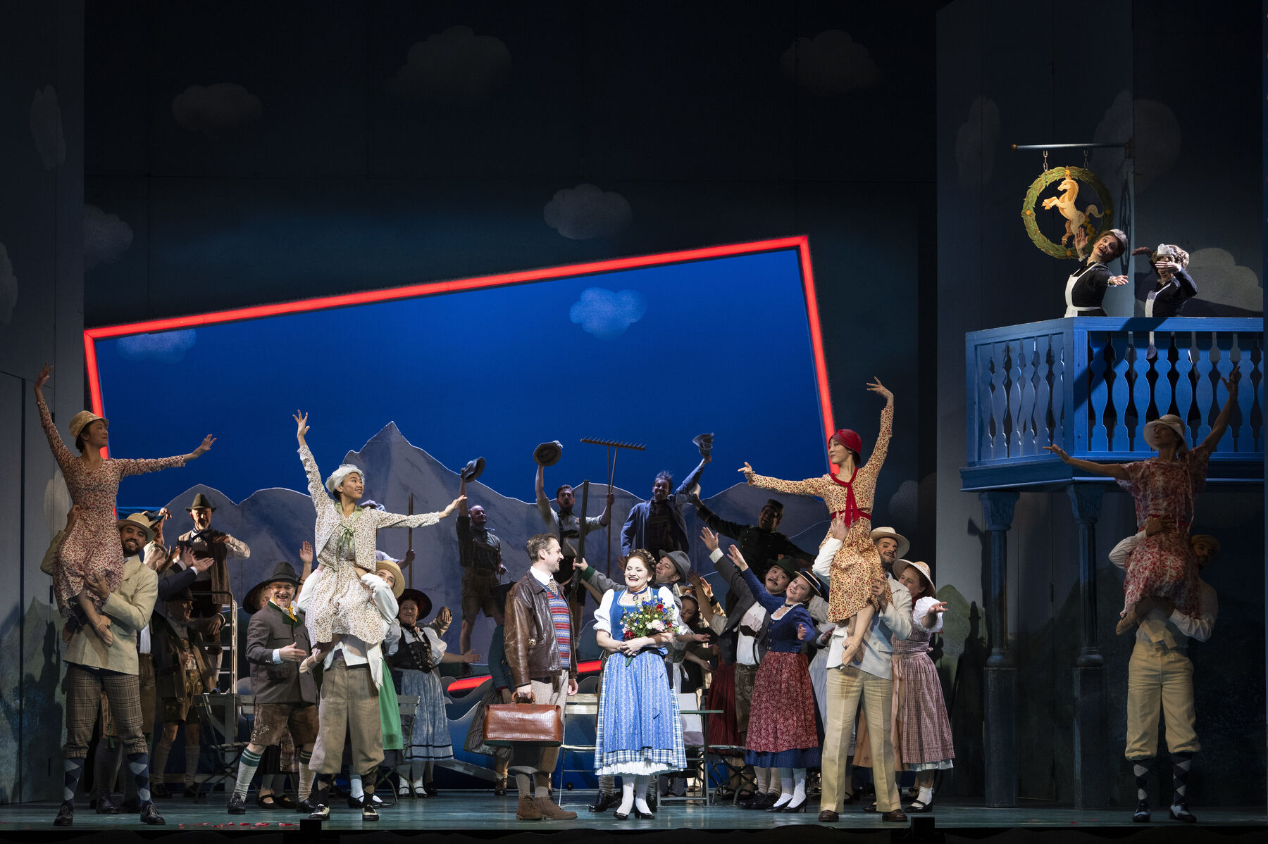 Darstellerinnen und das Ballettensemble sind auf der Bühne zu sehen. Im Hintergrund sieht man einen Blauen Rahmen.