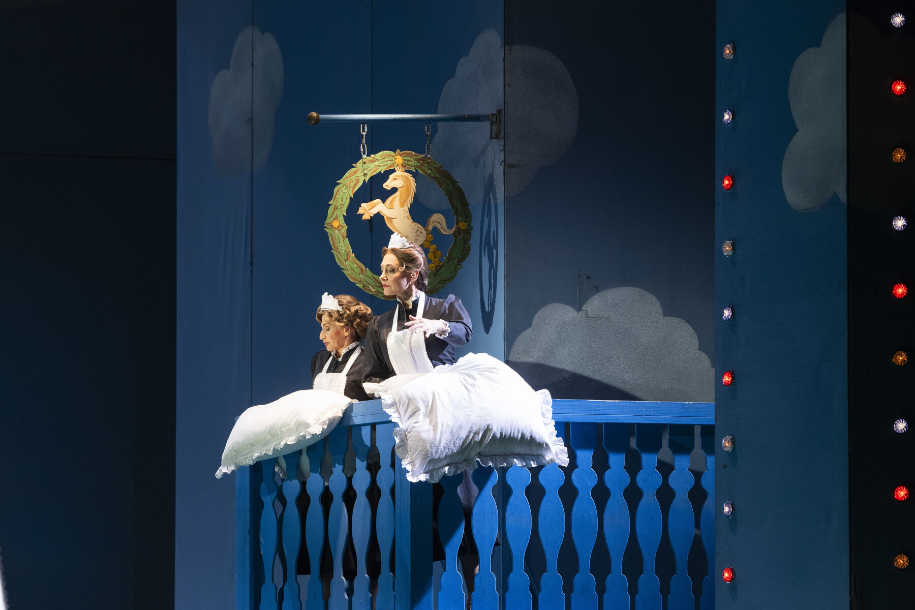 Zwei Frauen stehen auf einem blaue Balkon. Es liegen zwei weiße Kissen vor ihnen.