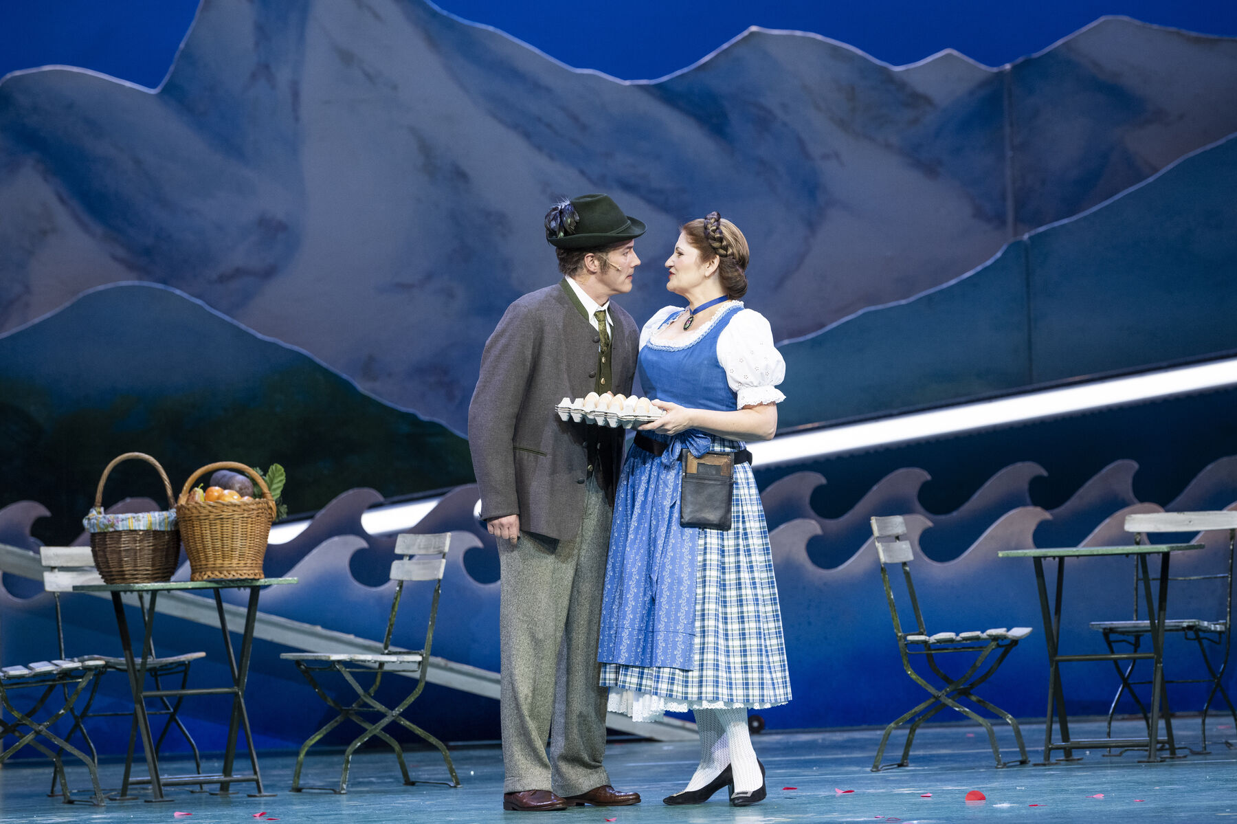 Ein Mann und eine Frau stehen auf der Bühne. Sie hat eier in der Hand. auf der Bühne stehen Stühle.