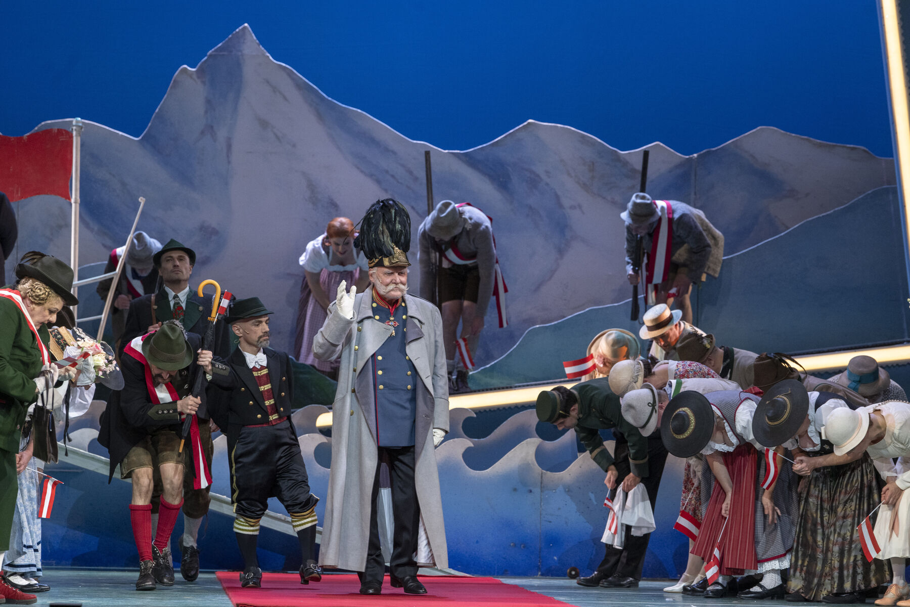 Mitglieder des Ensembles sind auf der blauen Bühne zu sehen. Im Hintergrund sind Berge.