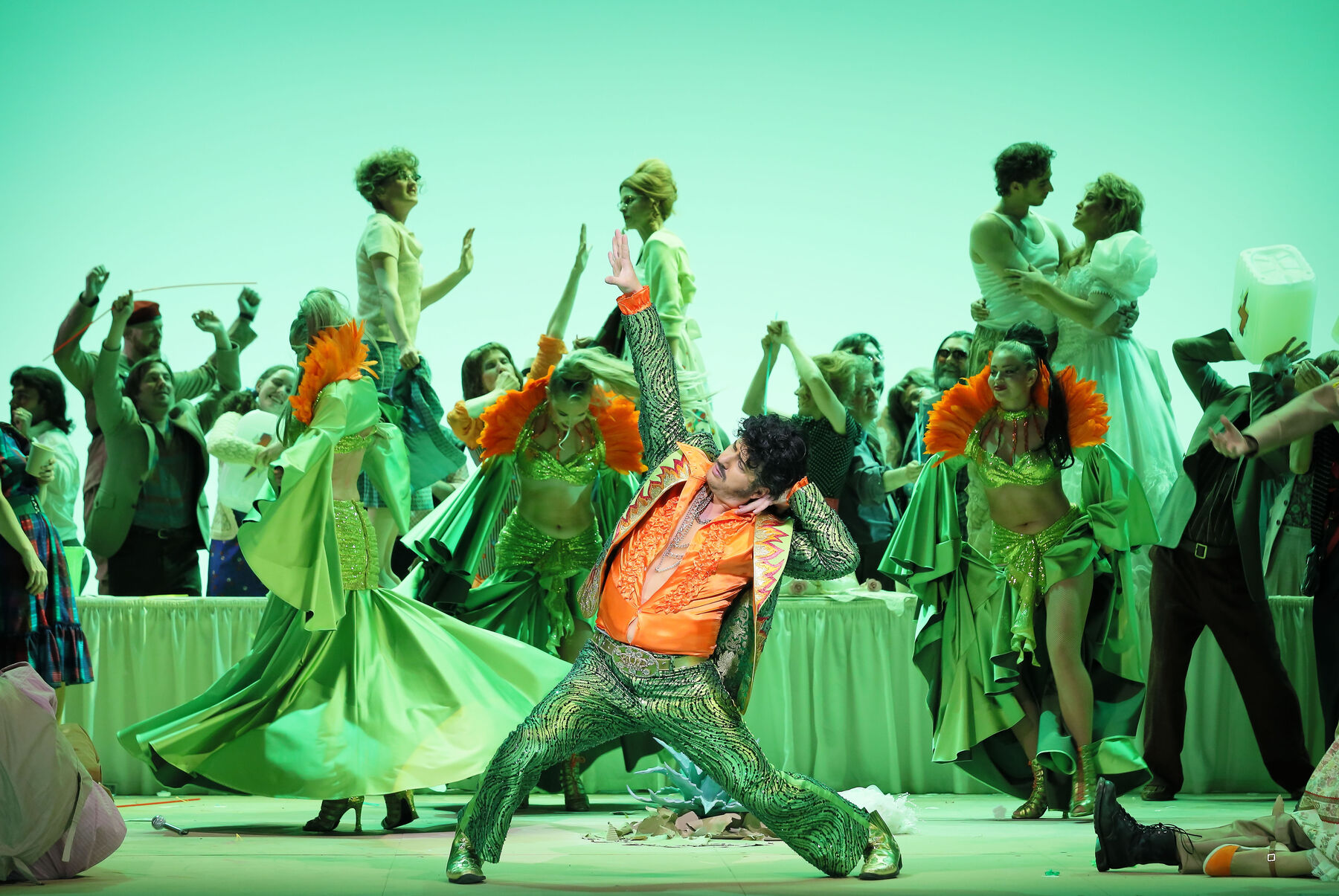 A dancing crowd, in front of them stands a man in a rocker outfit striking a dance pose.