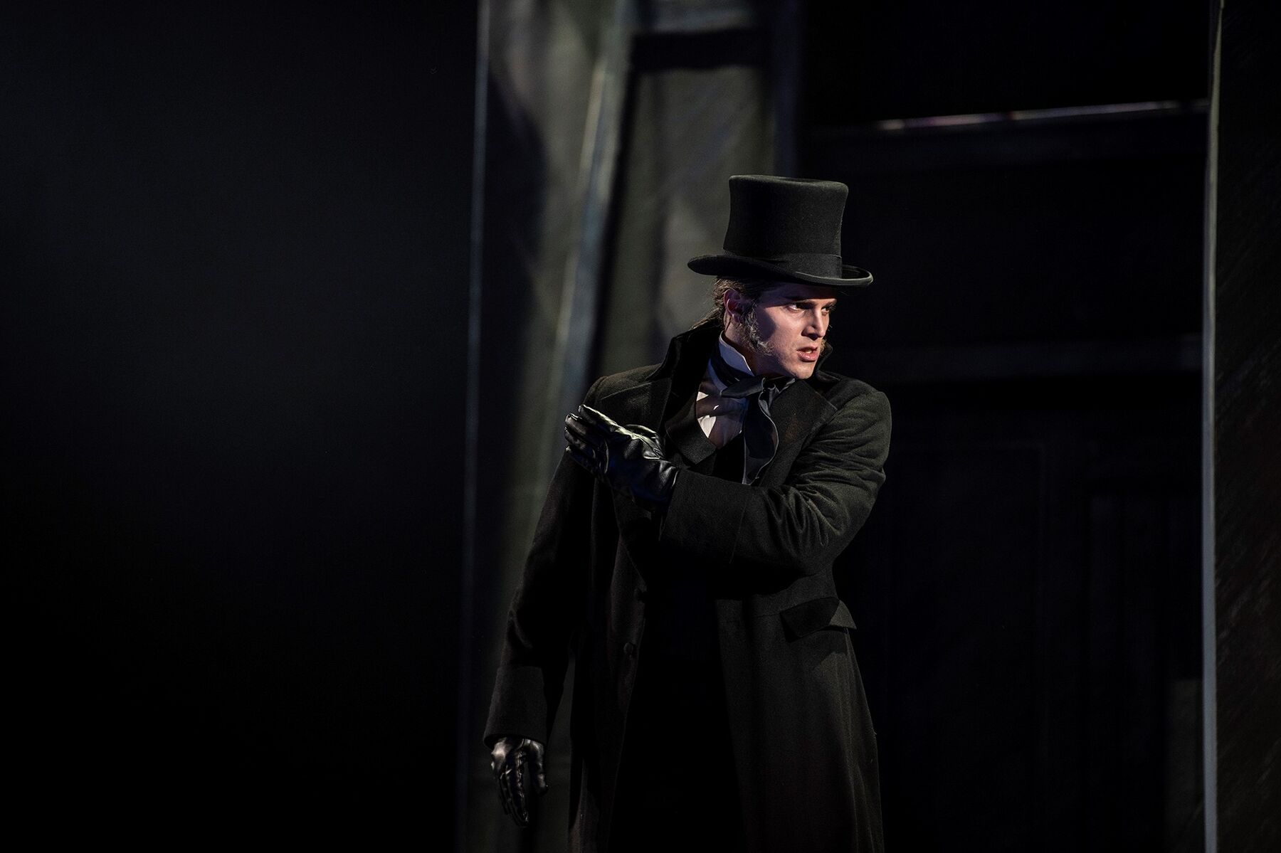 Javert mit schwarzem Zylinder und Mantel steht vor einem schwarzen Hintergrund.