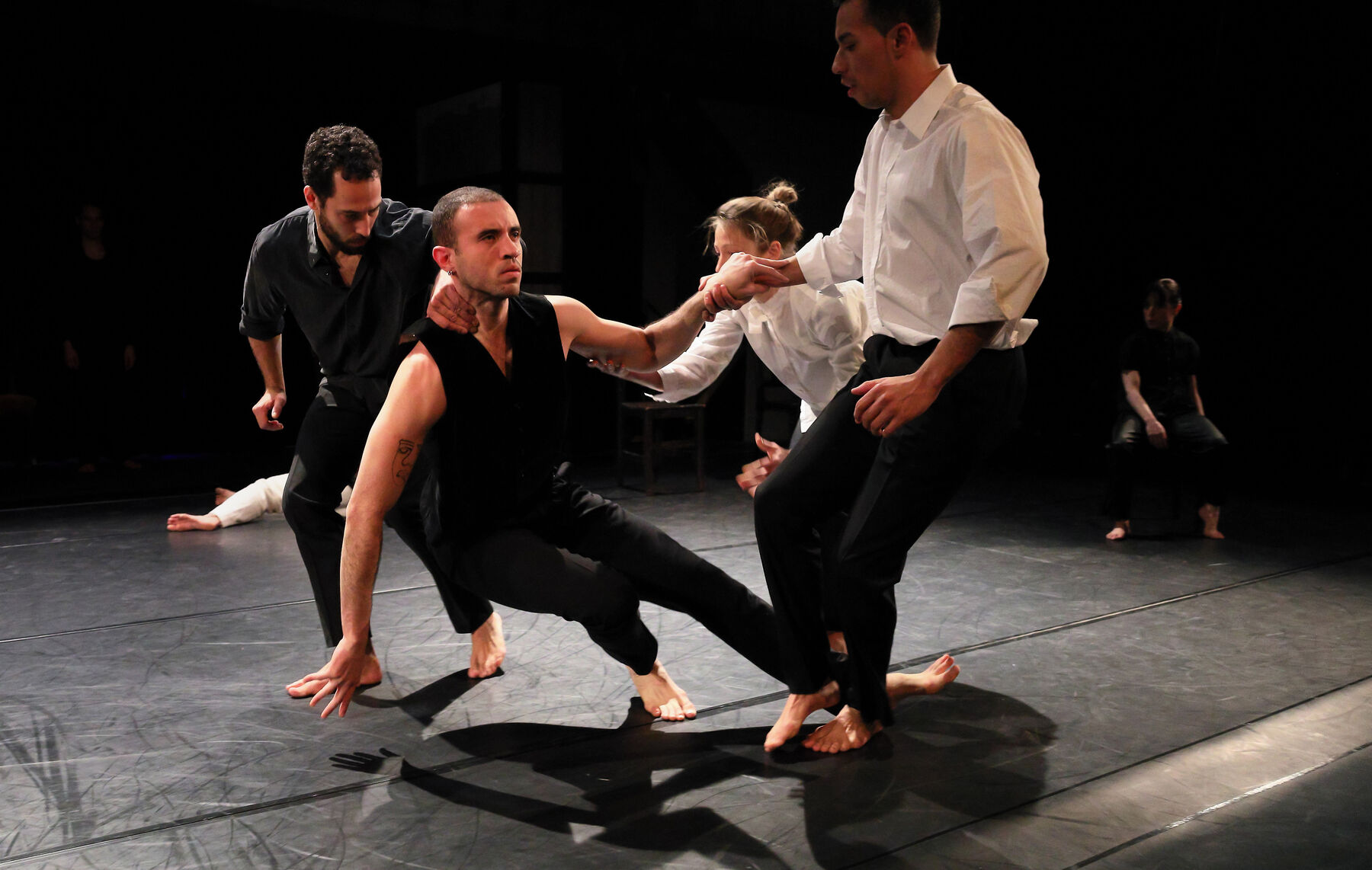 Four dancers, are dancing together. In the background can be seen other dancers.