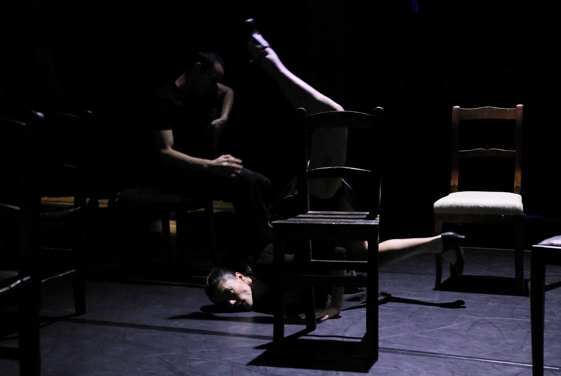 Chairs are standing in a dark room. Between a woman is dancing.