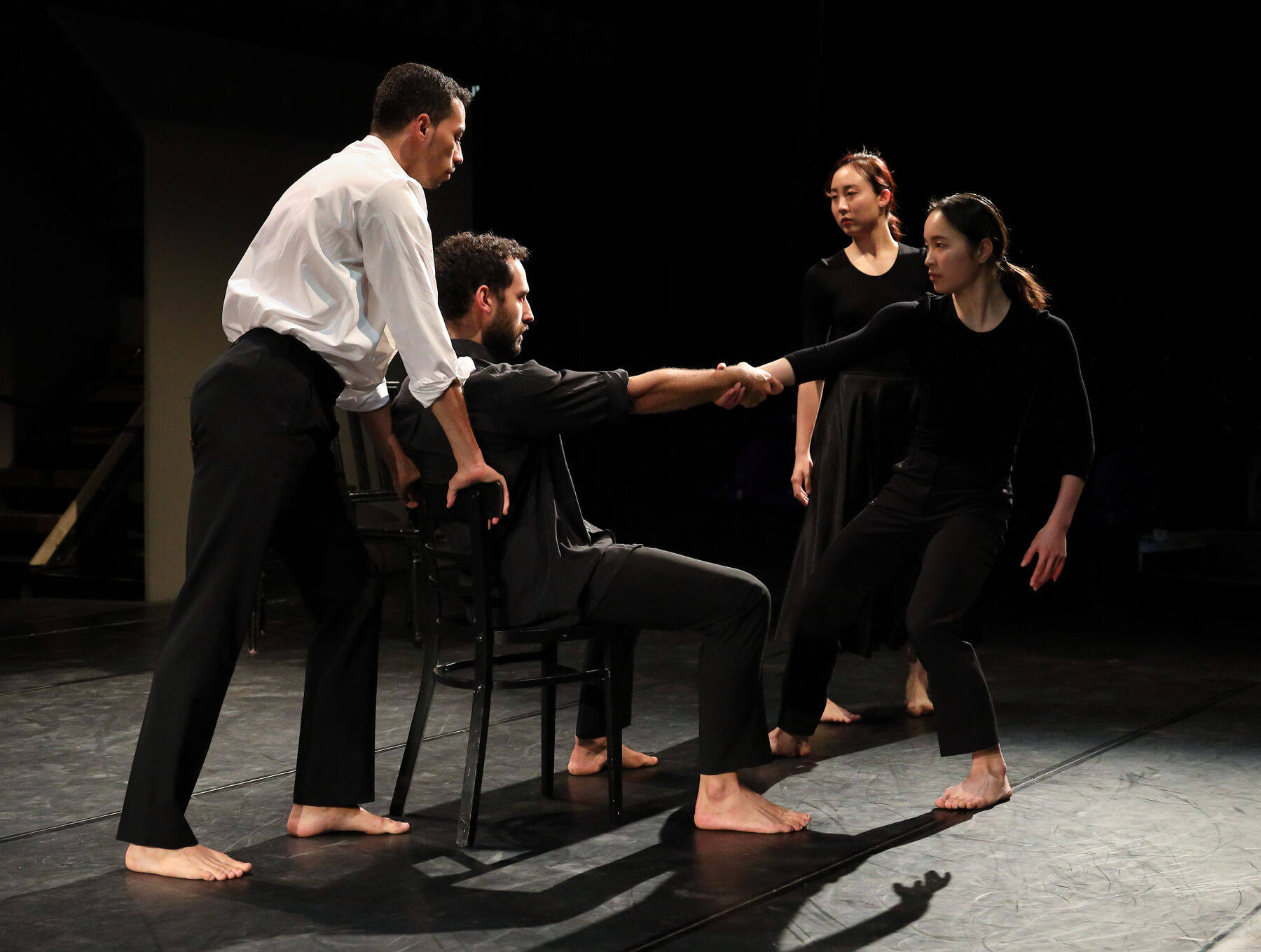 Four dancers, three dressed in black, one in white, can be seen.
