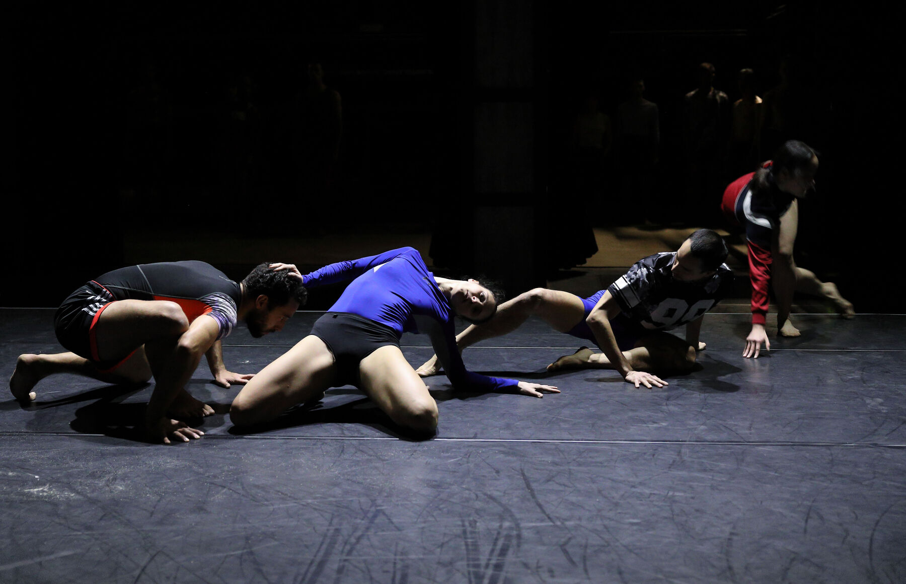 Four dancers can be seen in a dark room.