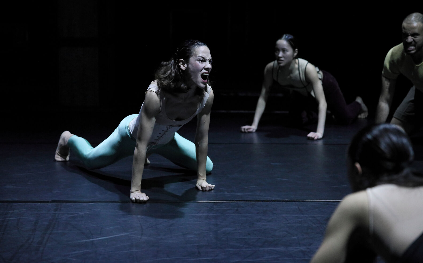 Dancers kneeeling on the floor in a dark room. they are screaming.