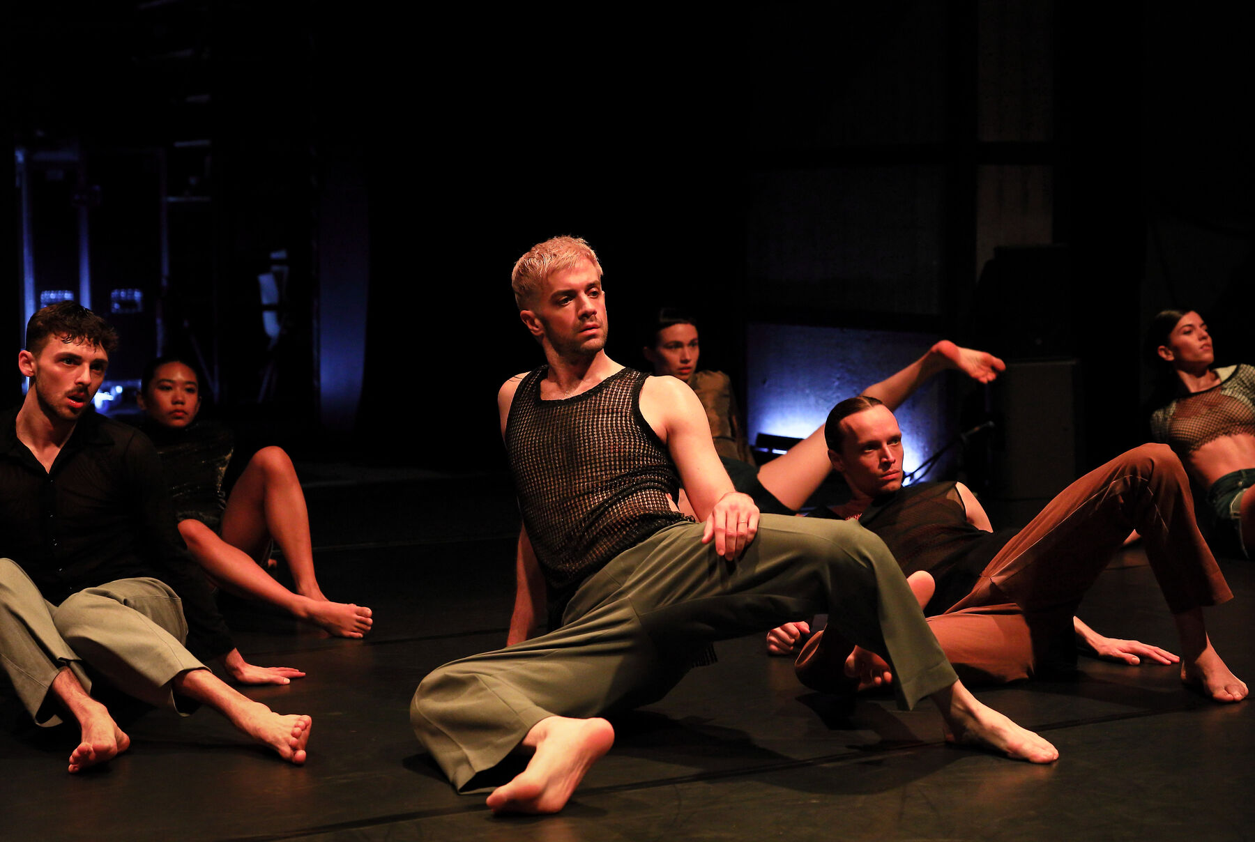 Dancers can be seen in a dark room. Onto their faces, red lights are shining.