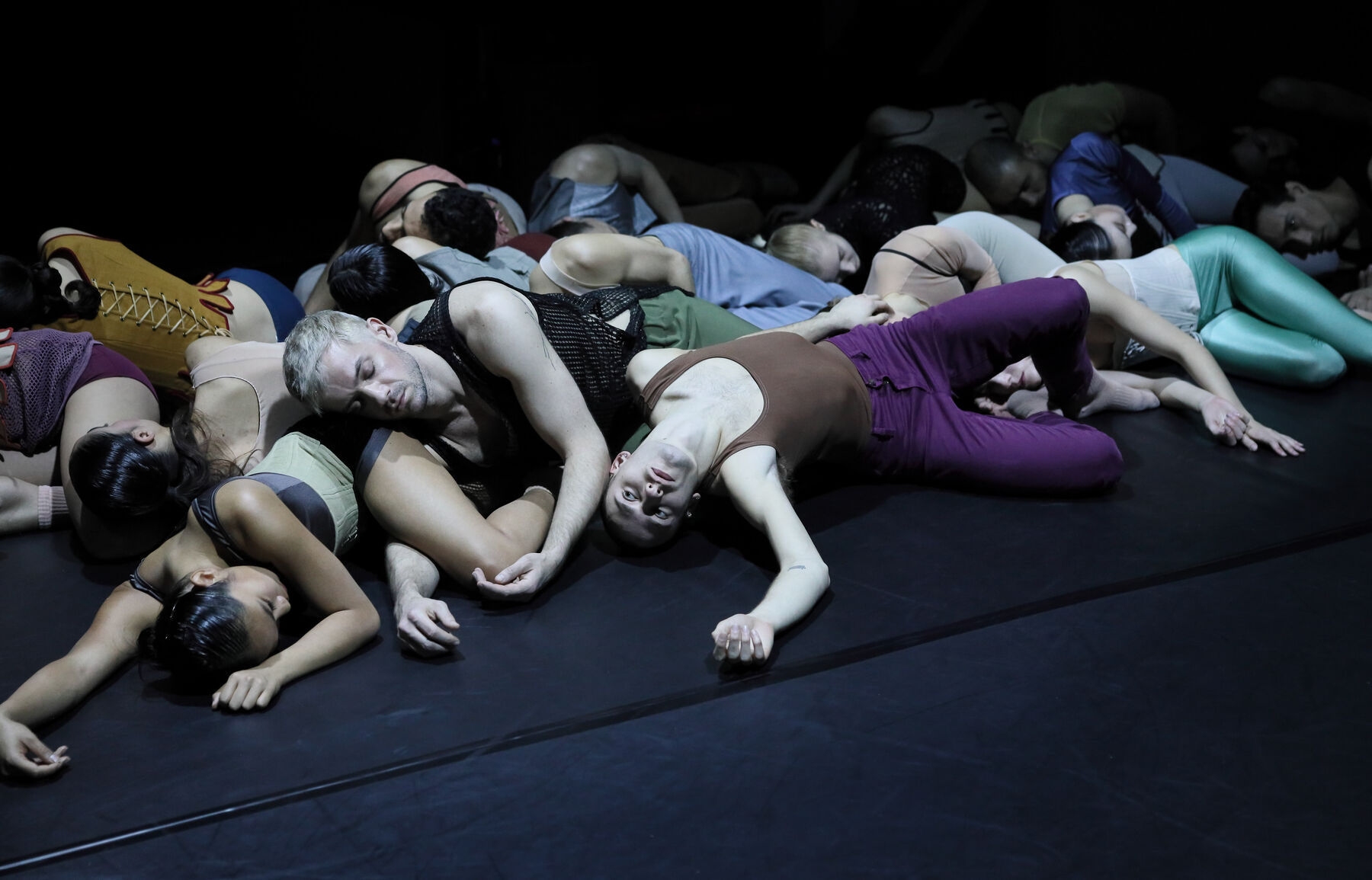 Dancers are lying on the floor in a dark room.