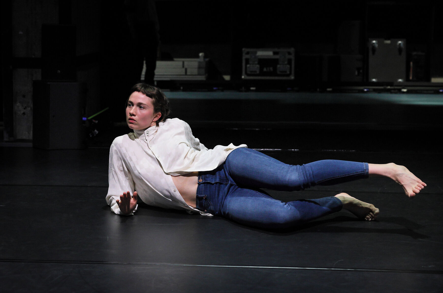 A Dancers is lying on the floor, dressed with jeans and a white blouse.