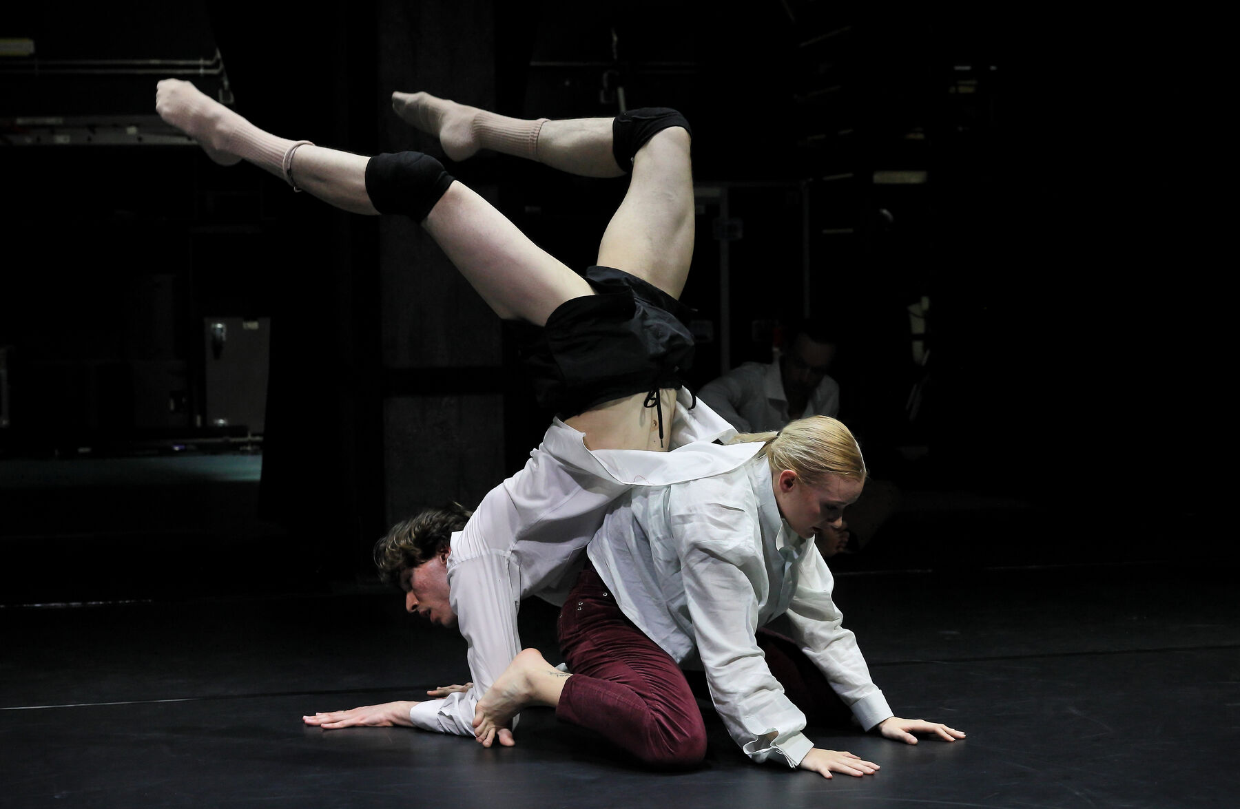 two dancers can be seen in a dark room, they dance together.