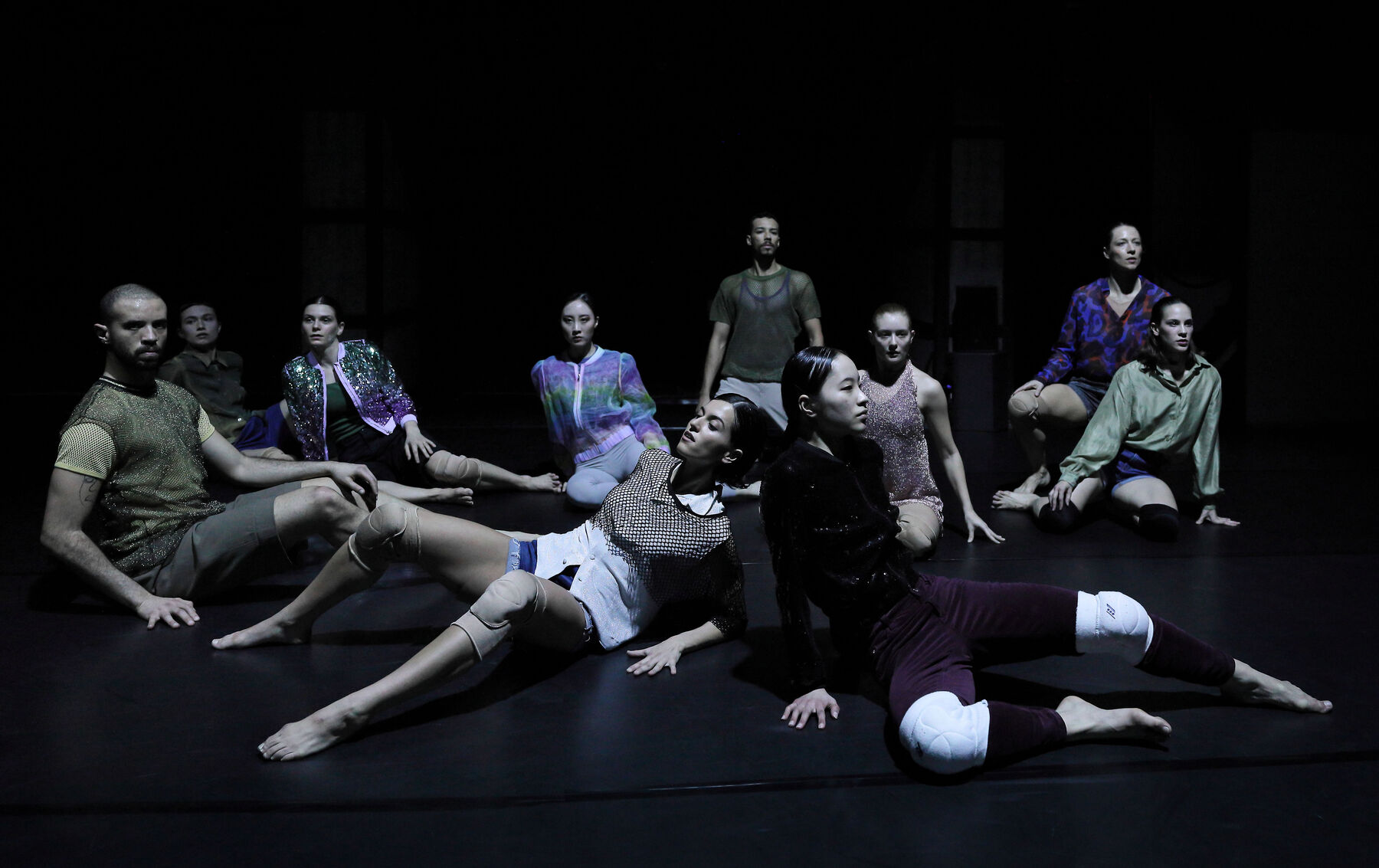 Dancers are sitting on the floor in a dark room.