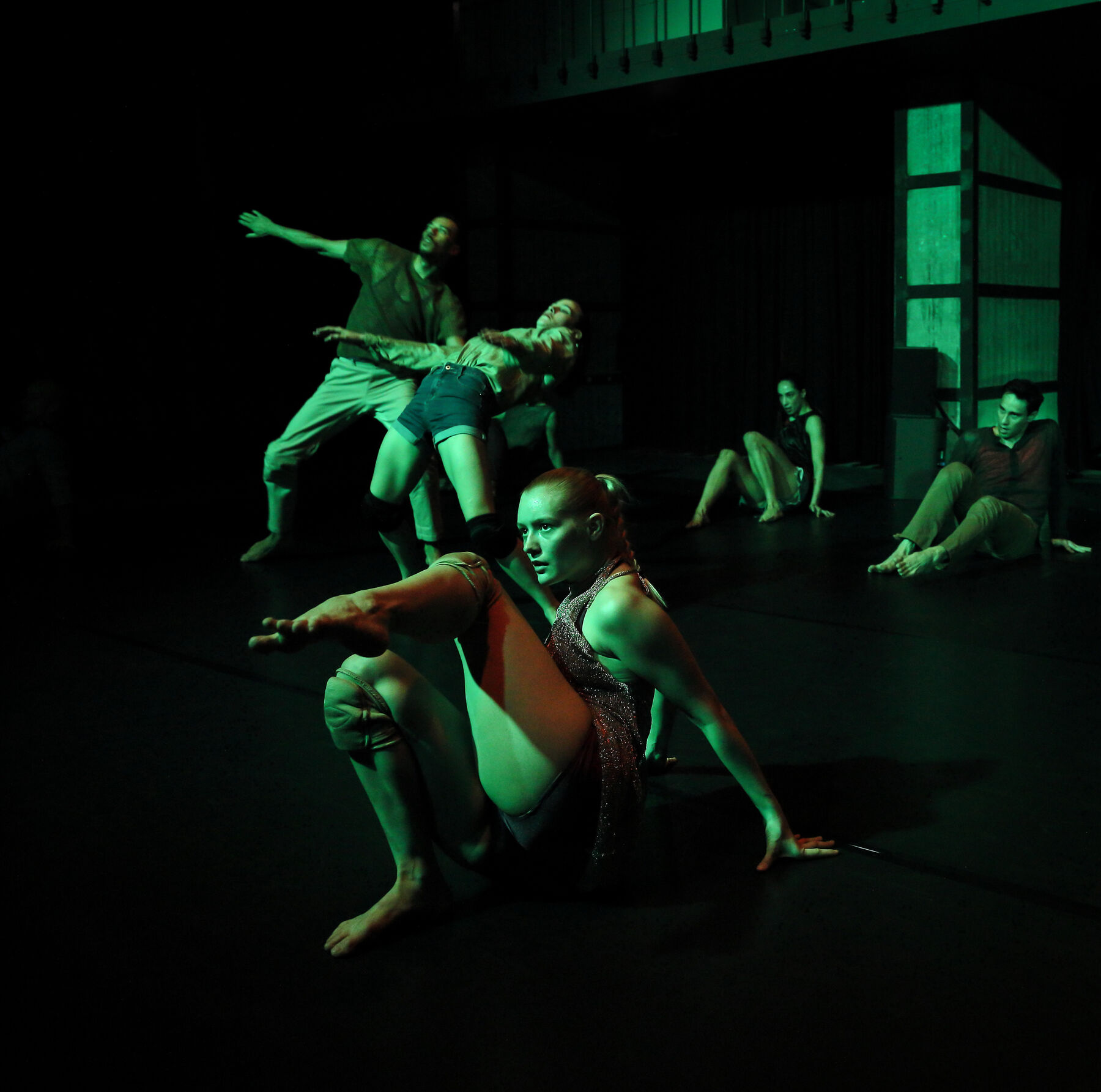 dancers can be seen in a dark room. Green light shines onto them.
