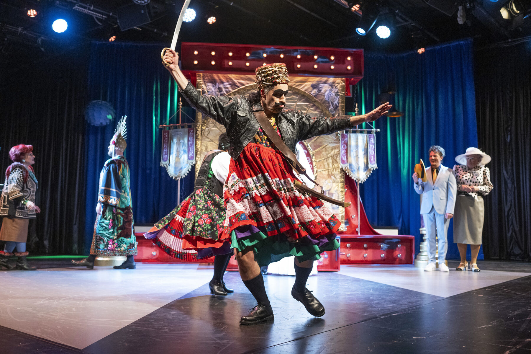 A man in skirts and a leather jacket dances with a sabre in his hand. There is an altar in the background and several people around the altar. 