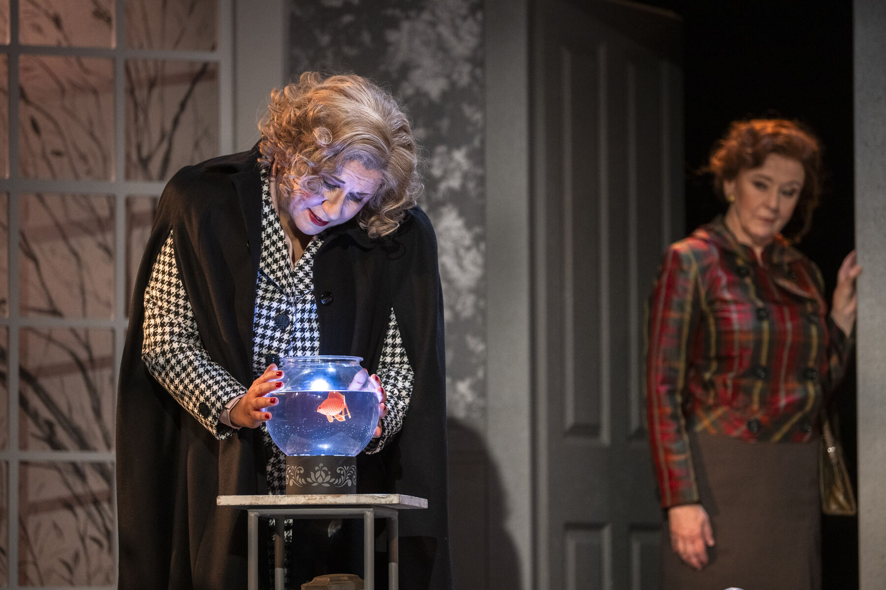 Miss Todd is saddened and lovingly strokes her goldfish bowl. In the background, Miss Pinkerton stands in the doorway.