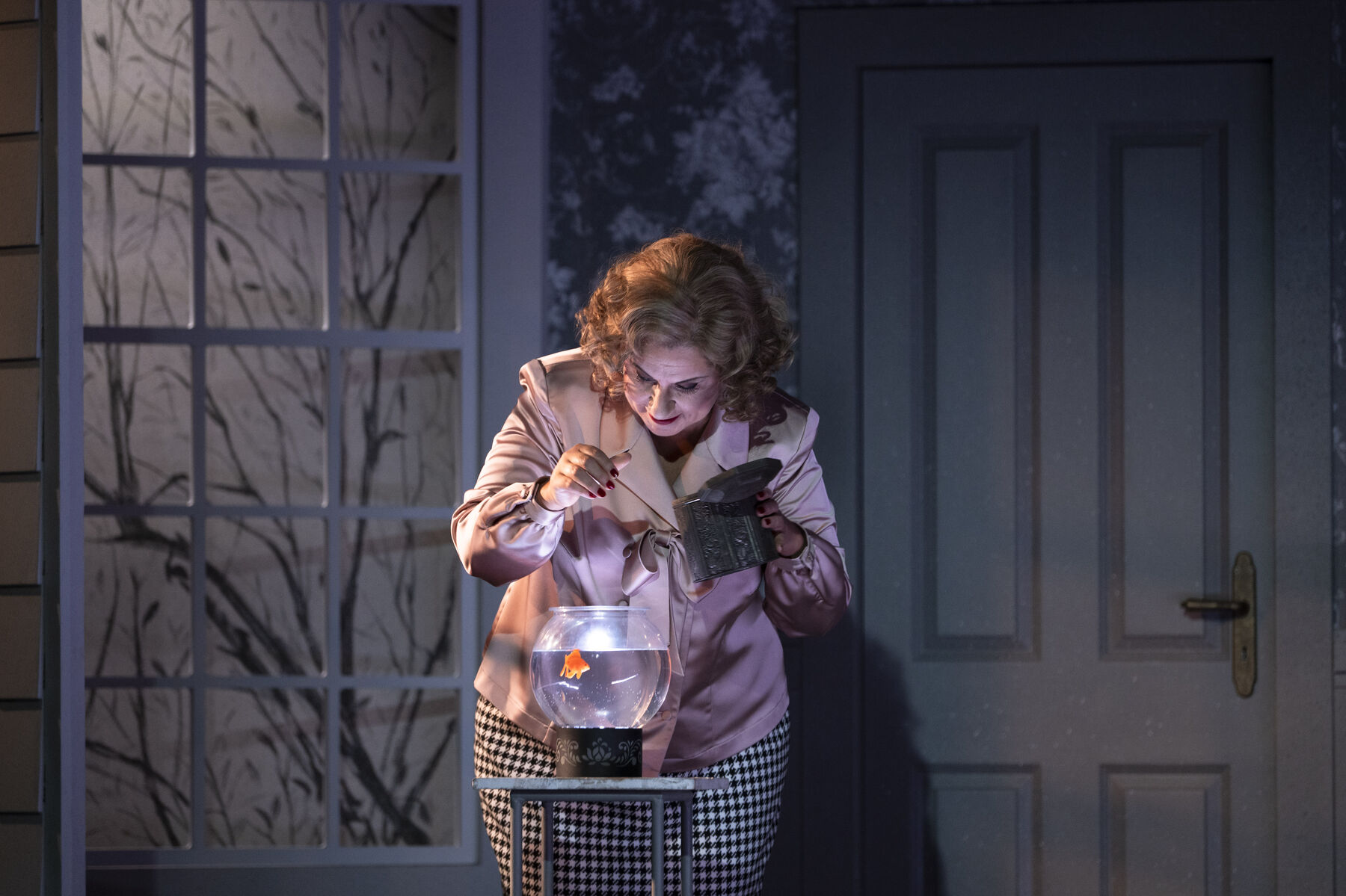 Miss Todd feeds her goldfish. The goldfish bowl stands on a small side table.