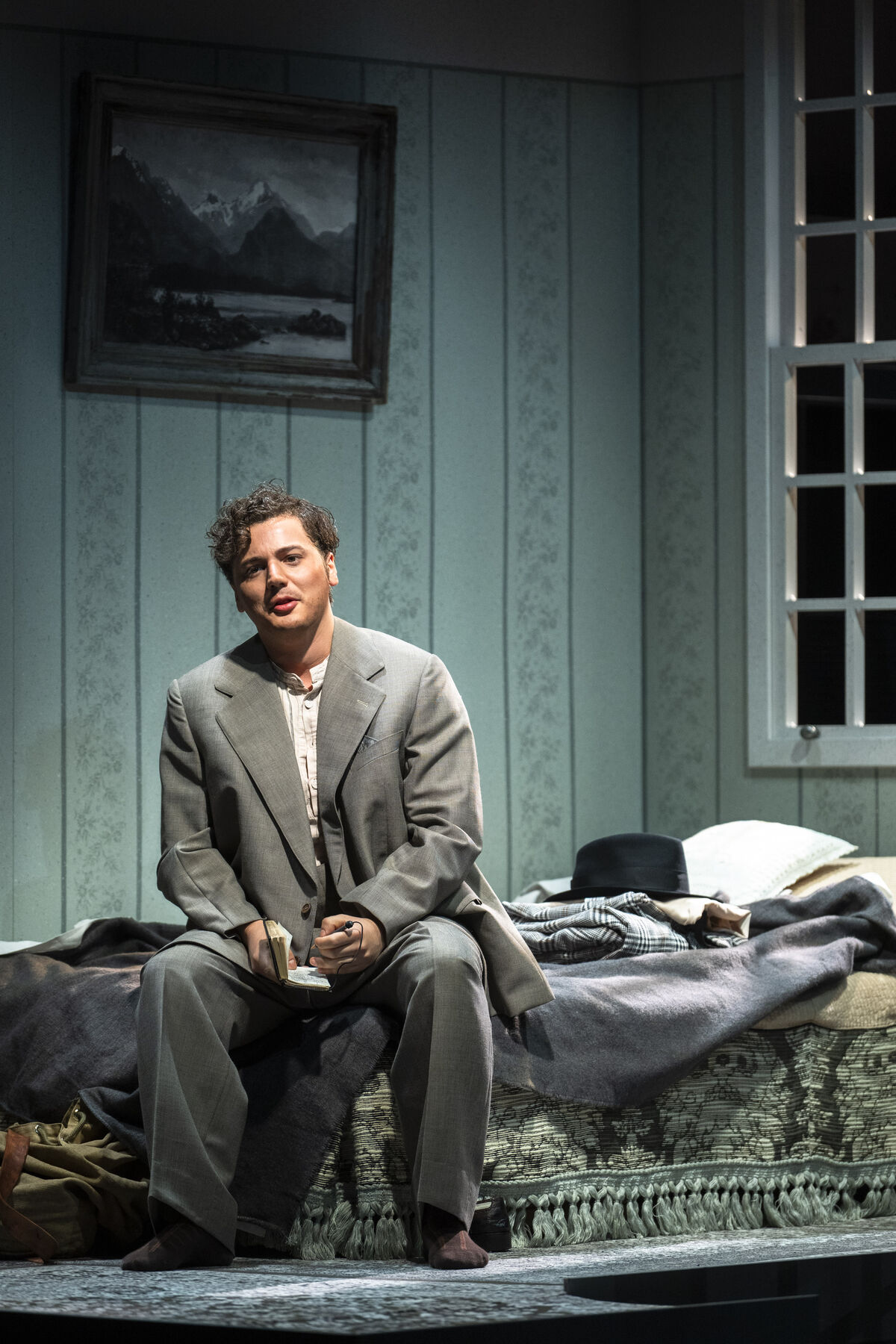 Bob is sitting on his bed writing something in a small notebook. He is wearing a grey suit.