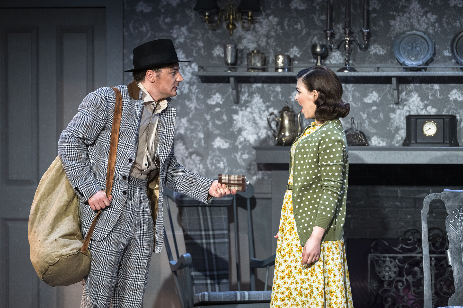Bob is ready to leave. He is wearing a black and white checked suit, a black hat and a rucksack on his back. His expression is tense. He holds out a purse to Laetitia. She is visibly surprised.