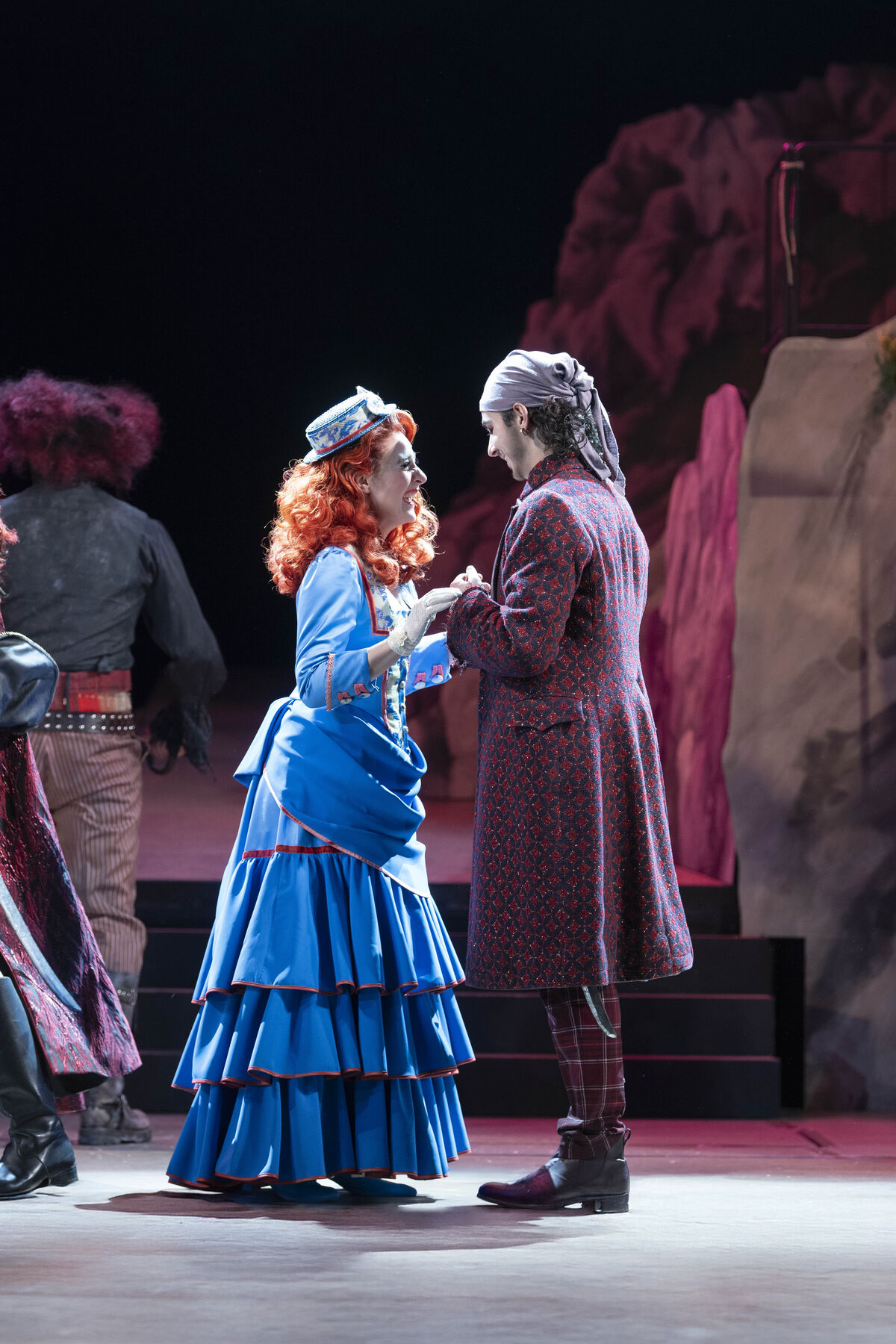 The young pirate Frederic holds Mabel's hands as they stand facing each other. Both are happy, and she laughs exuberantly.