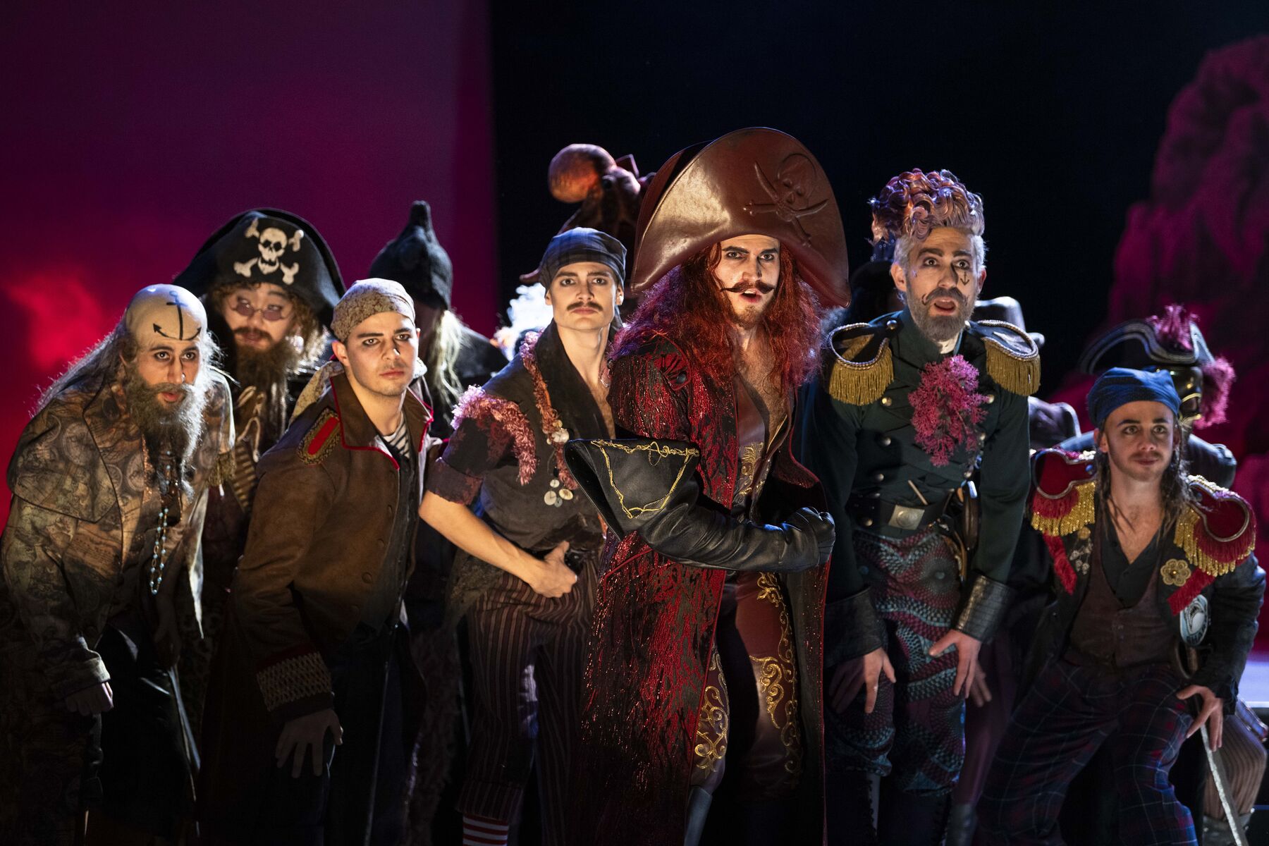 Pirate king Richard looks determinedly ahead. His pirate crew, including his assistant Samuel, stand united behind him. The light is reddish, lending the scene an air of menace.