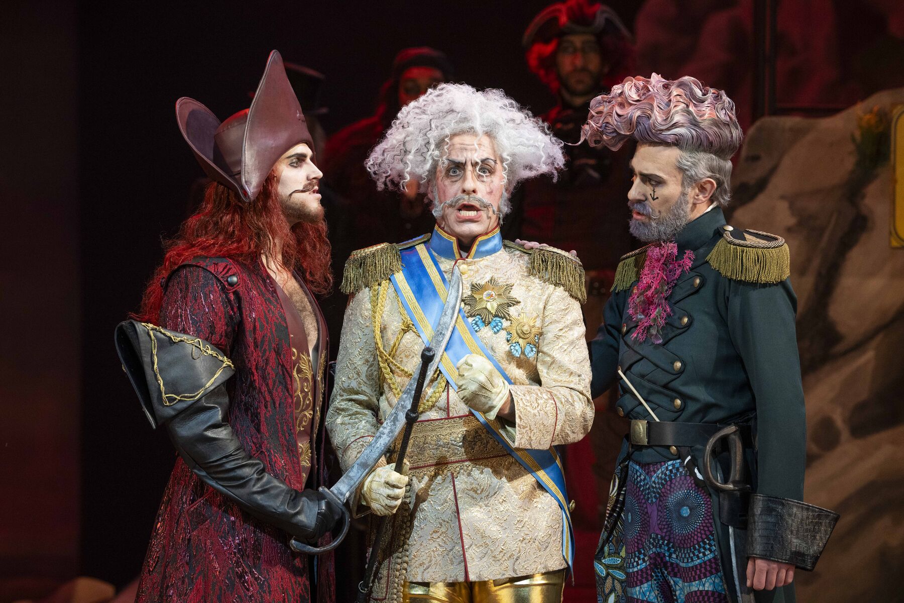 The pirate king and his assistant threaten Major General Stanley with their sabres. The major general is terrified. More pirates can be seen in the background. 