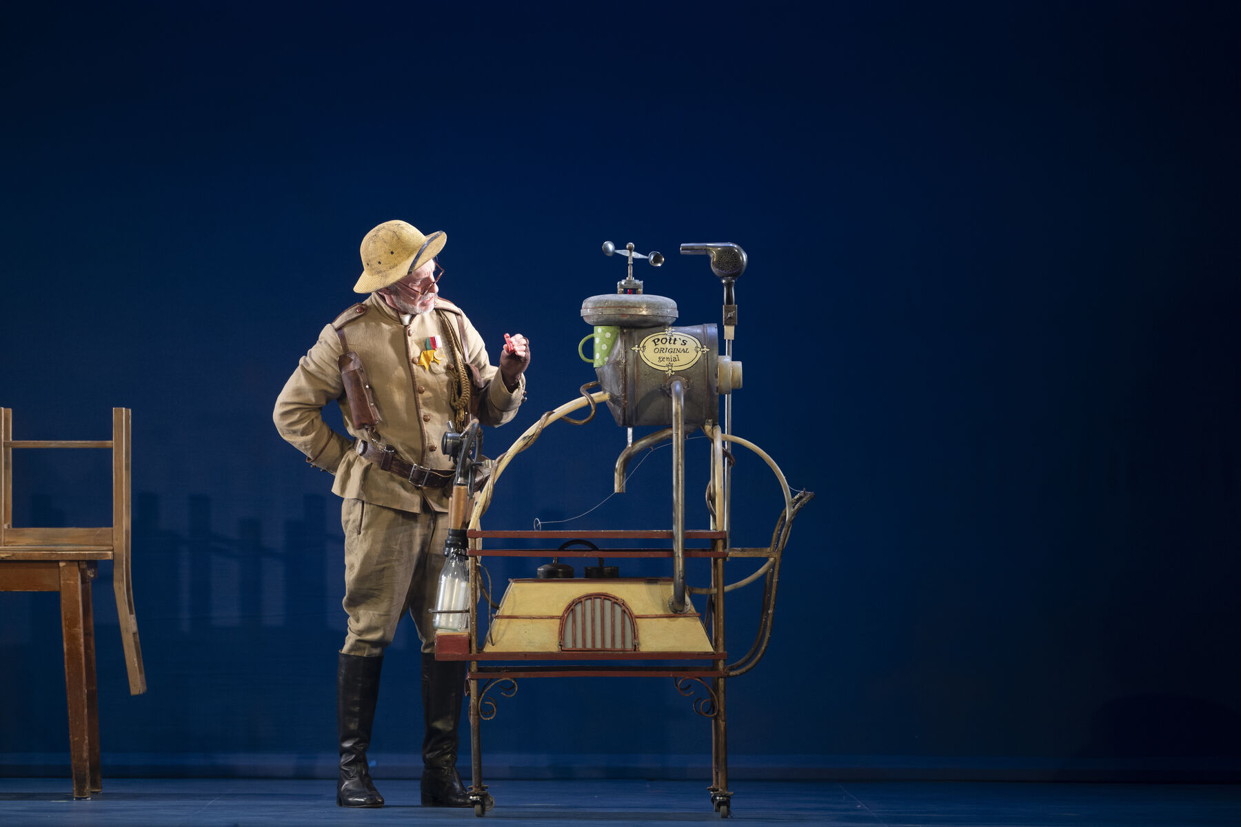An elderly gentleman in uniform stands in front of a machine and sceptically examines a small red object.