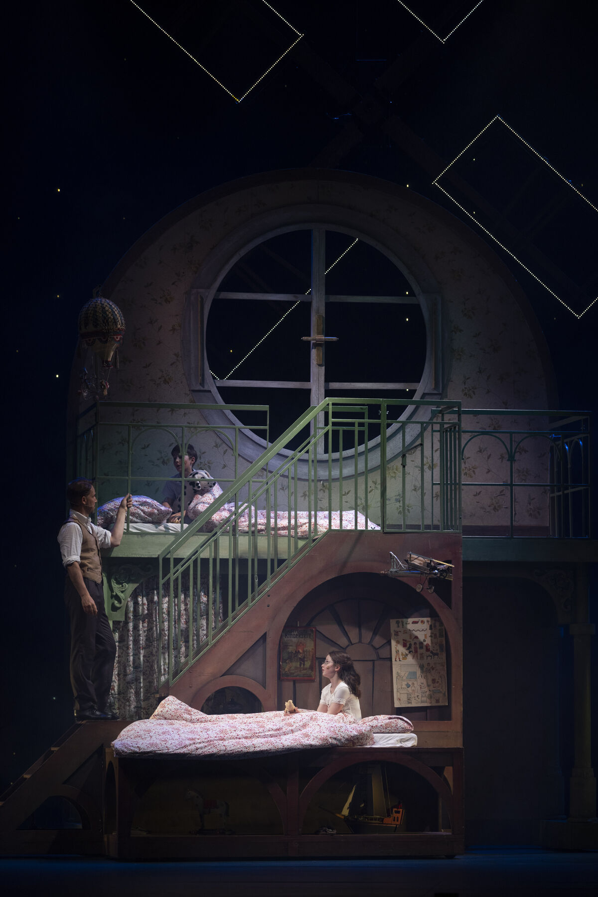 A man is standing on a staircase. At the top, a boy is sitting in his bed and looking at him. At the bottom, a girl is sitting in her bed and also looking at the man. The scene is rather dark, with stars visible in the background.
