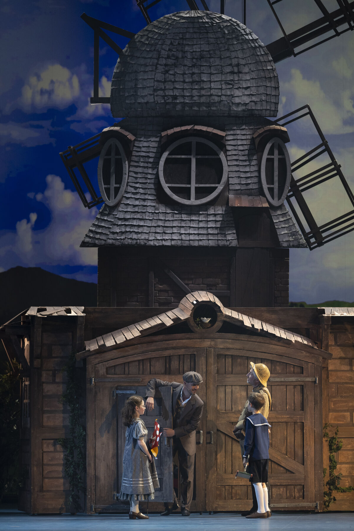 An older man and a younger man are standing in front of a windmill with two children.