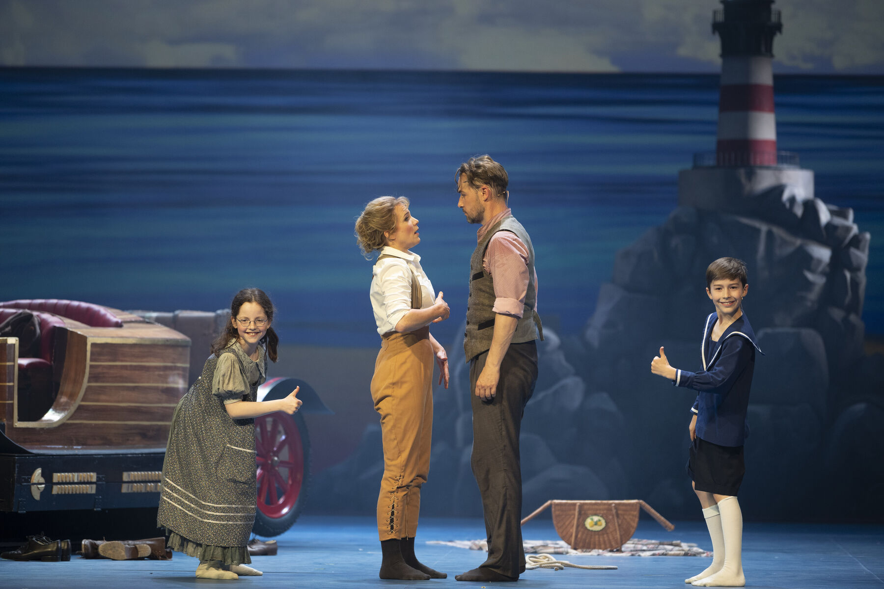 A man and a woman stand facing each other and look into each other's eyes. Behind her stands a girl and behind him a boy. The two children grin and give a ‘thumbs up’ sign. In the background, a car stands by the sea.