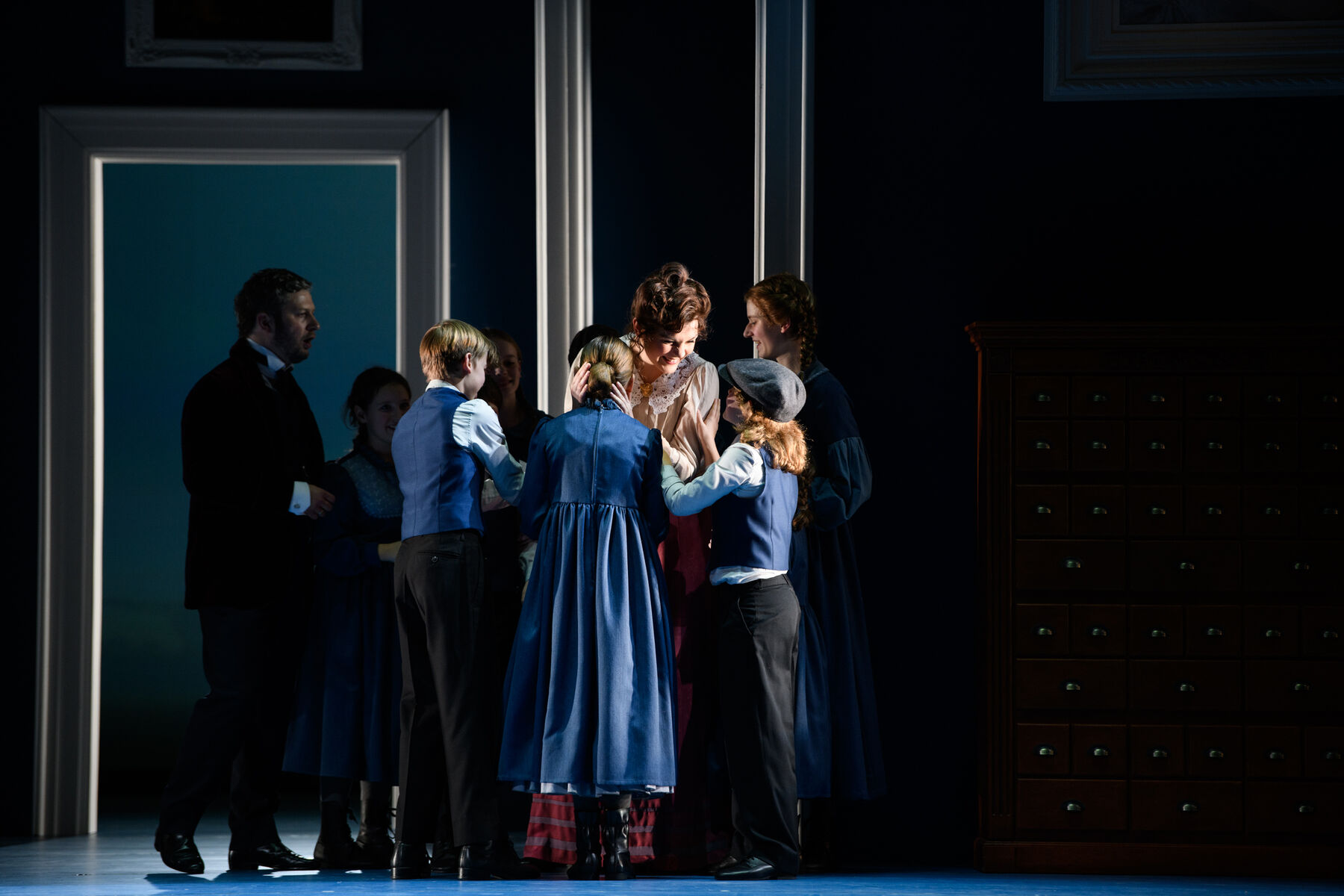 Eine Frau umarmt eine Gruppe kleiner Kinder, die sie anlächelt.